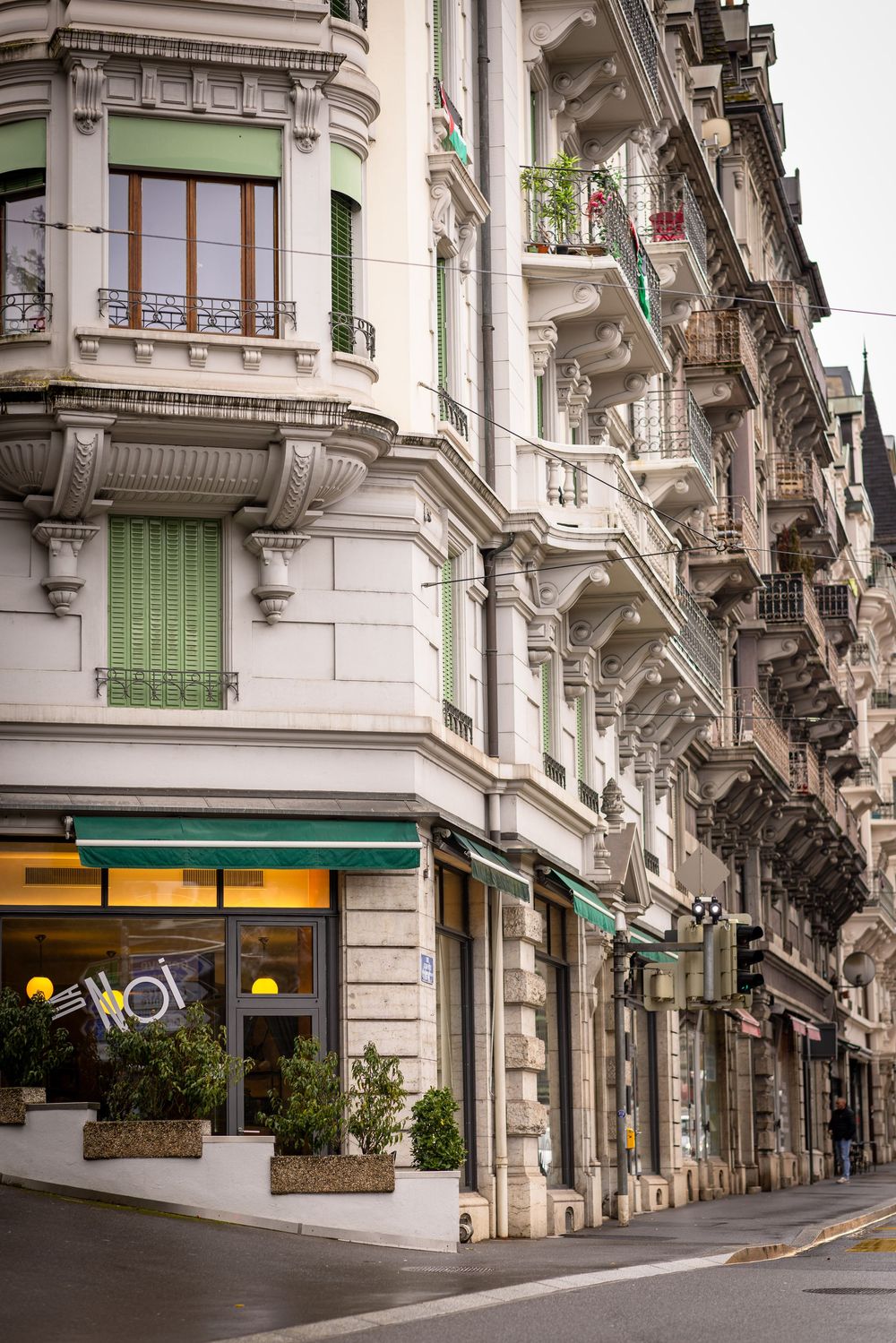 Elegant European building facade with classic architecture and green shutters featuring a restaurant storefront.