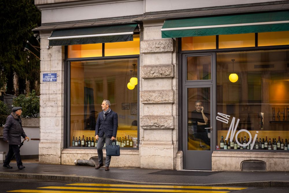 A person walks past a storefront window display at dusk with warm interior lighting glowing from inside.