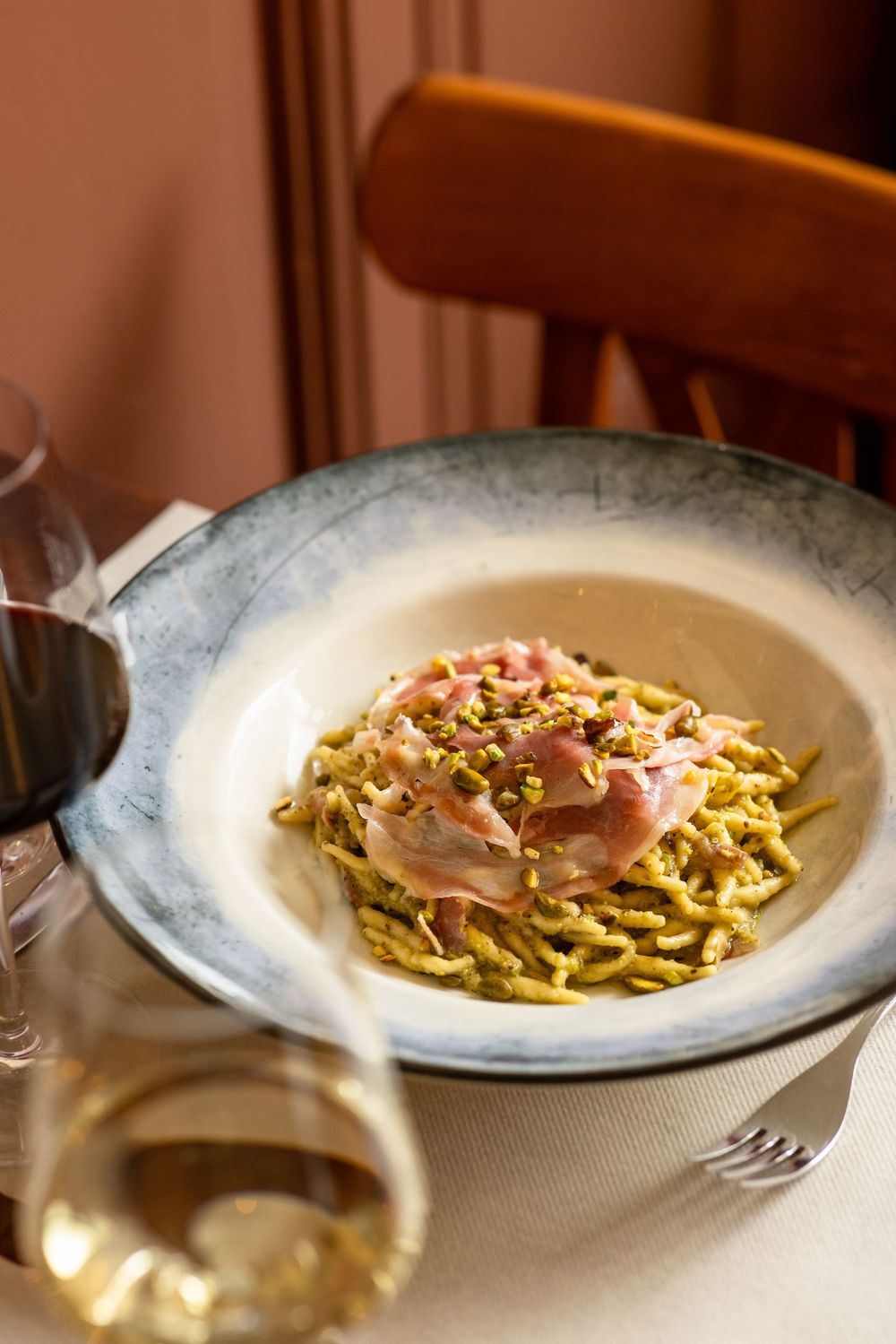 Freshly plated pasta dish with thin prosciutto slices and green herbs served on an elegant white plate.