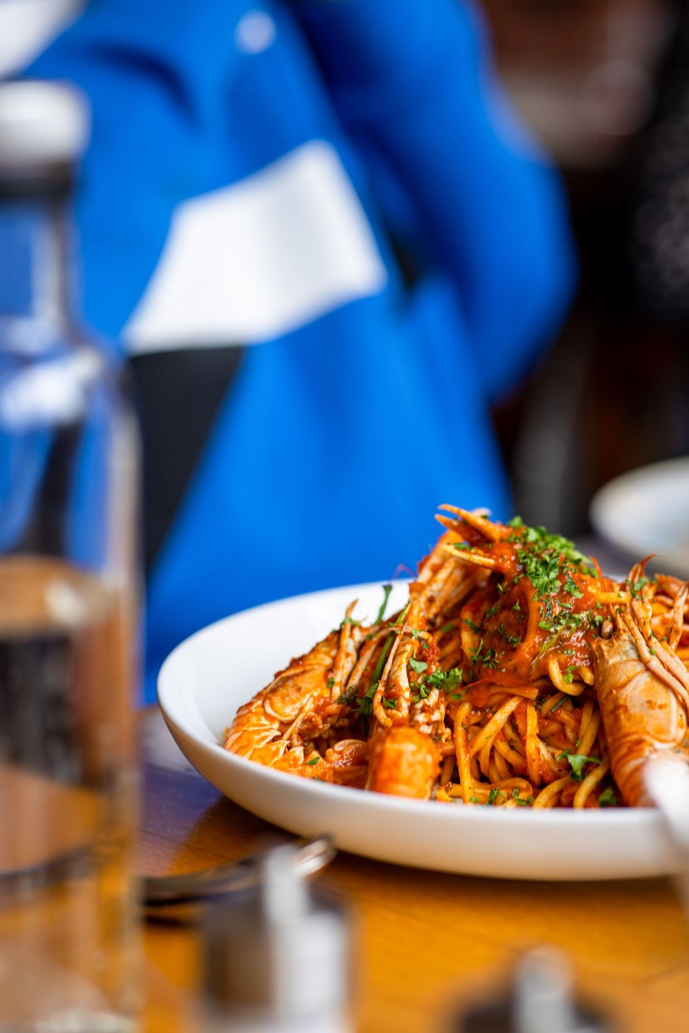 A plate of spicy shrimp pasta with noodles and garnish served on a wooden table with a blue background.