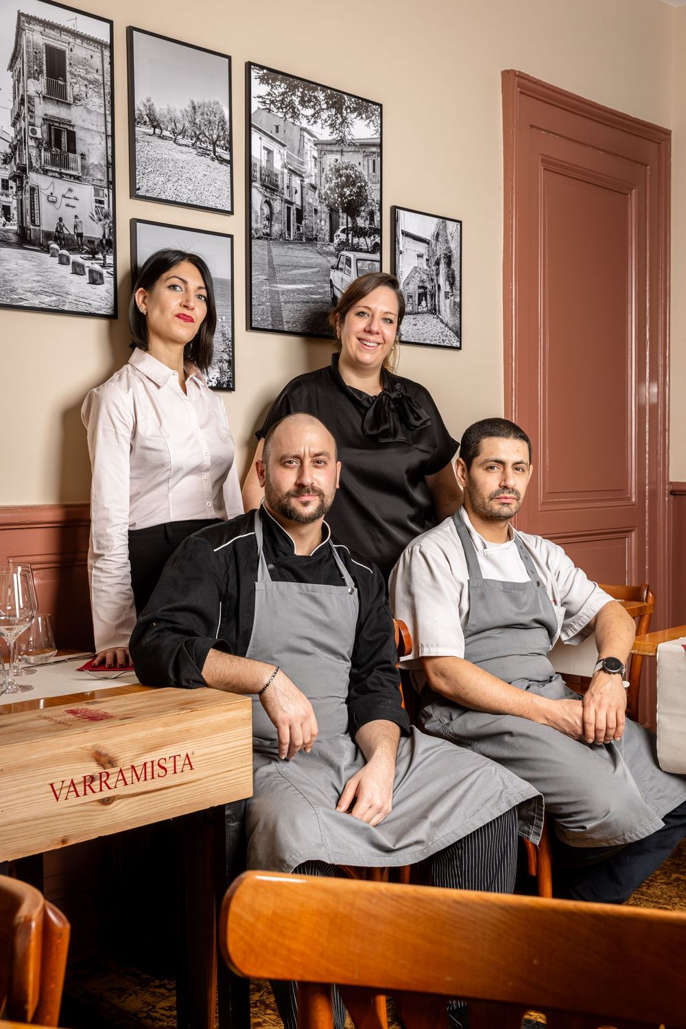 Restaurant staff members sitting together on wooden bench with black and white photos on wall behind them.