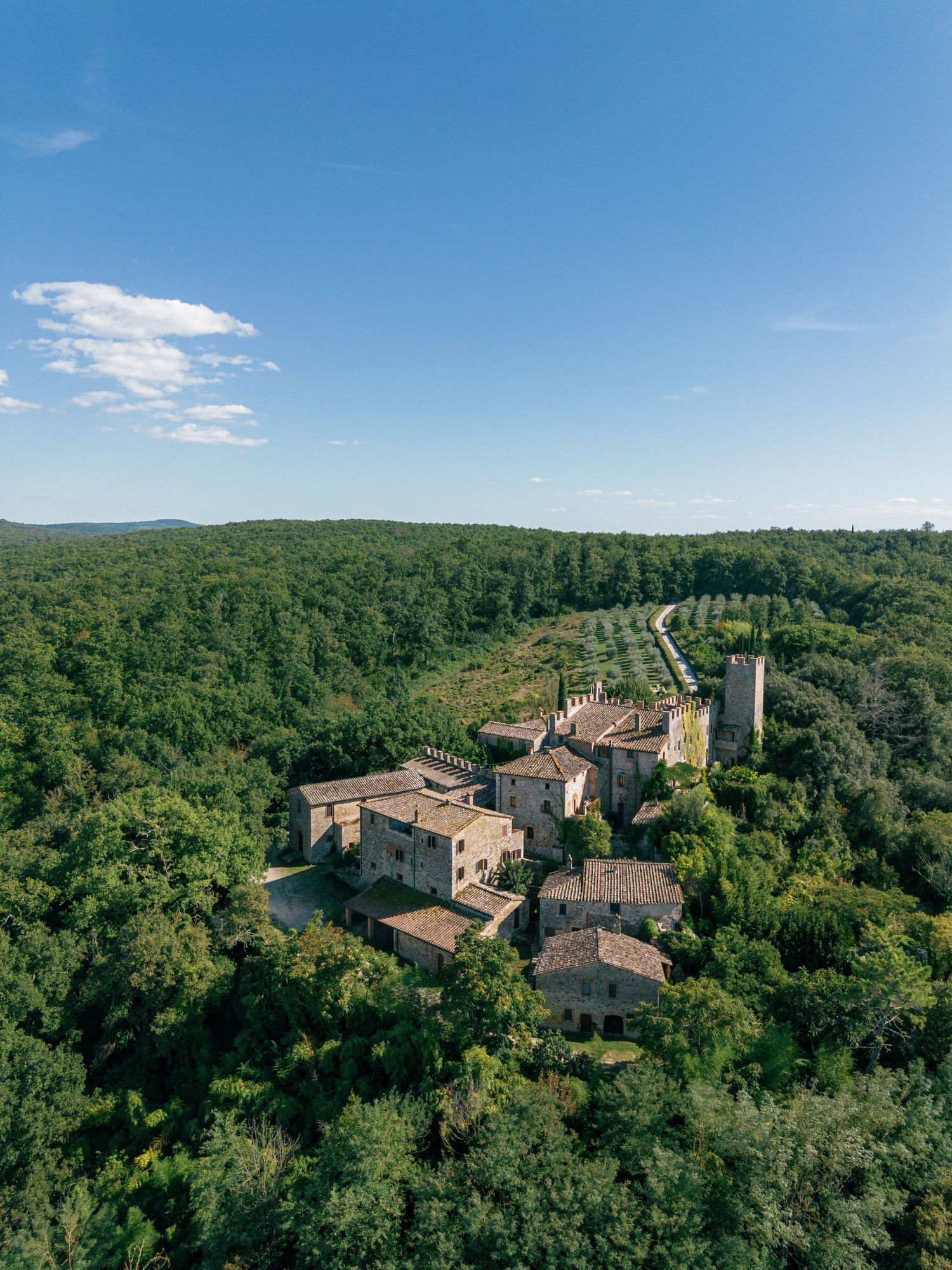 Panoramic aerial view of an ancient stone village nestled among lush green forests under bright blue skies.