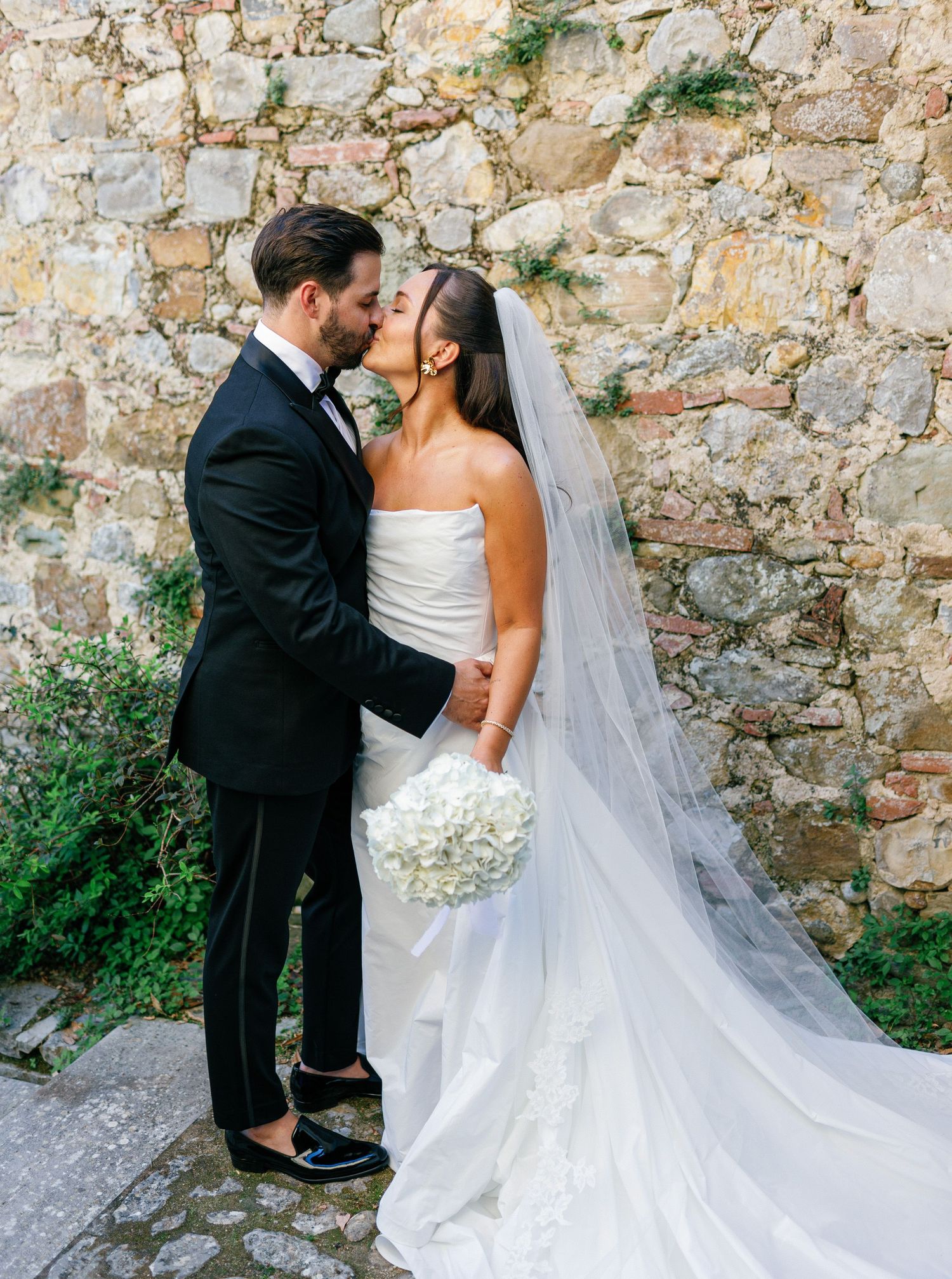 A romantic wedding couple poses against a rustic stone wall in a series of intimate portraits.