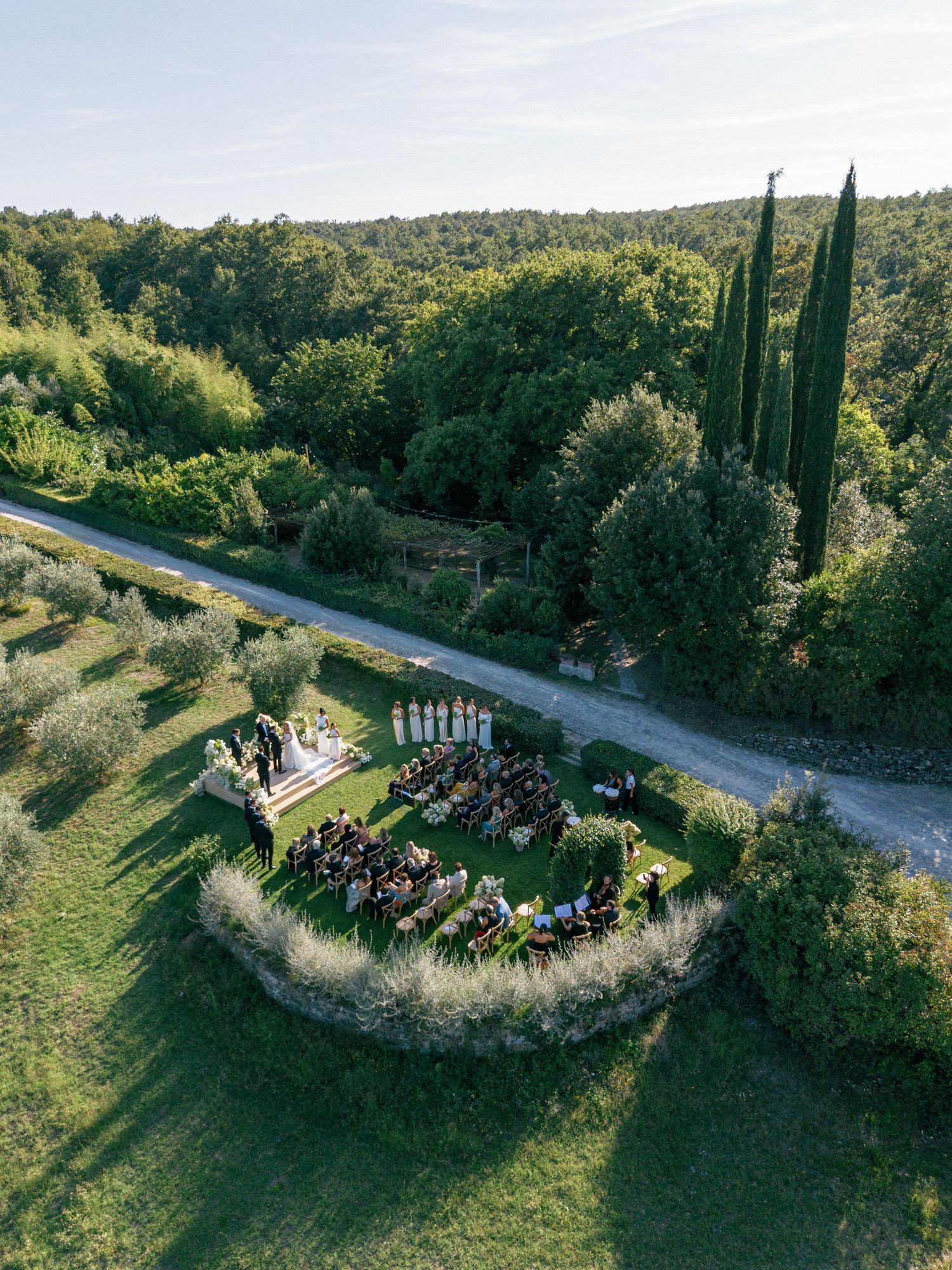 Aerial drone shots showing a gathering of people in a garden corner surrounded by cypress trees and greenery.