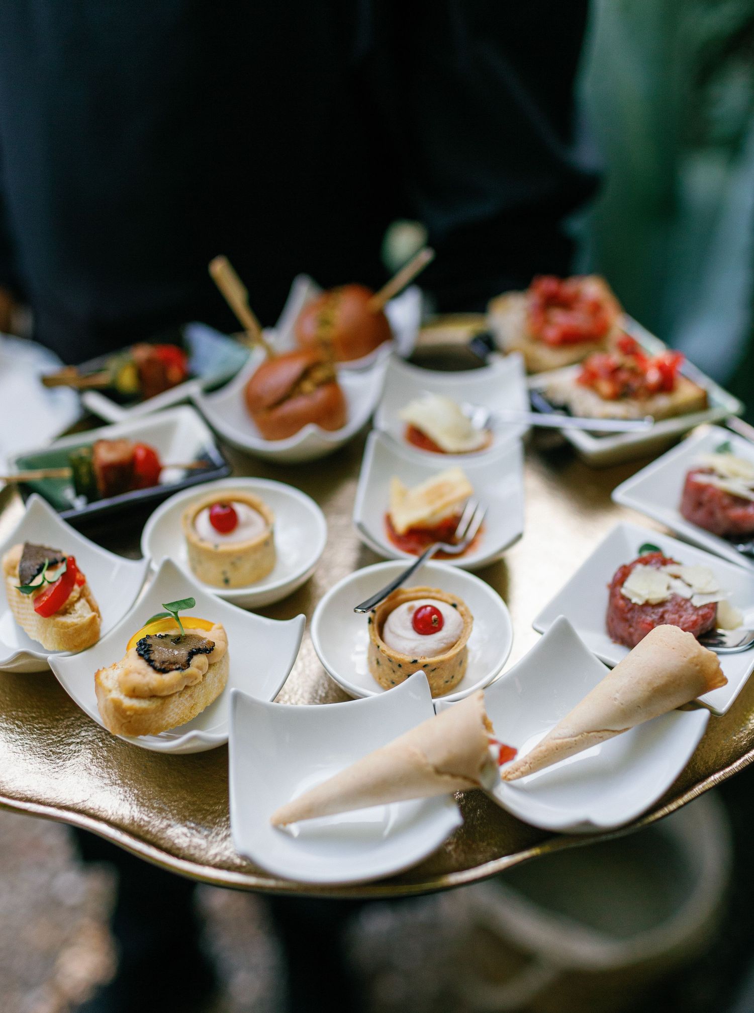 Elegant appetizers arranged on white ceramic spoons displayed on a reflective serving platter at a catered event.