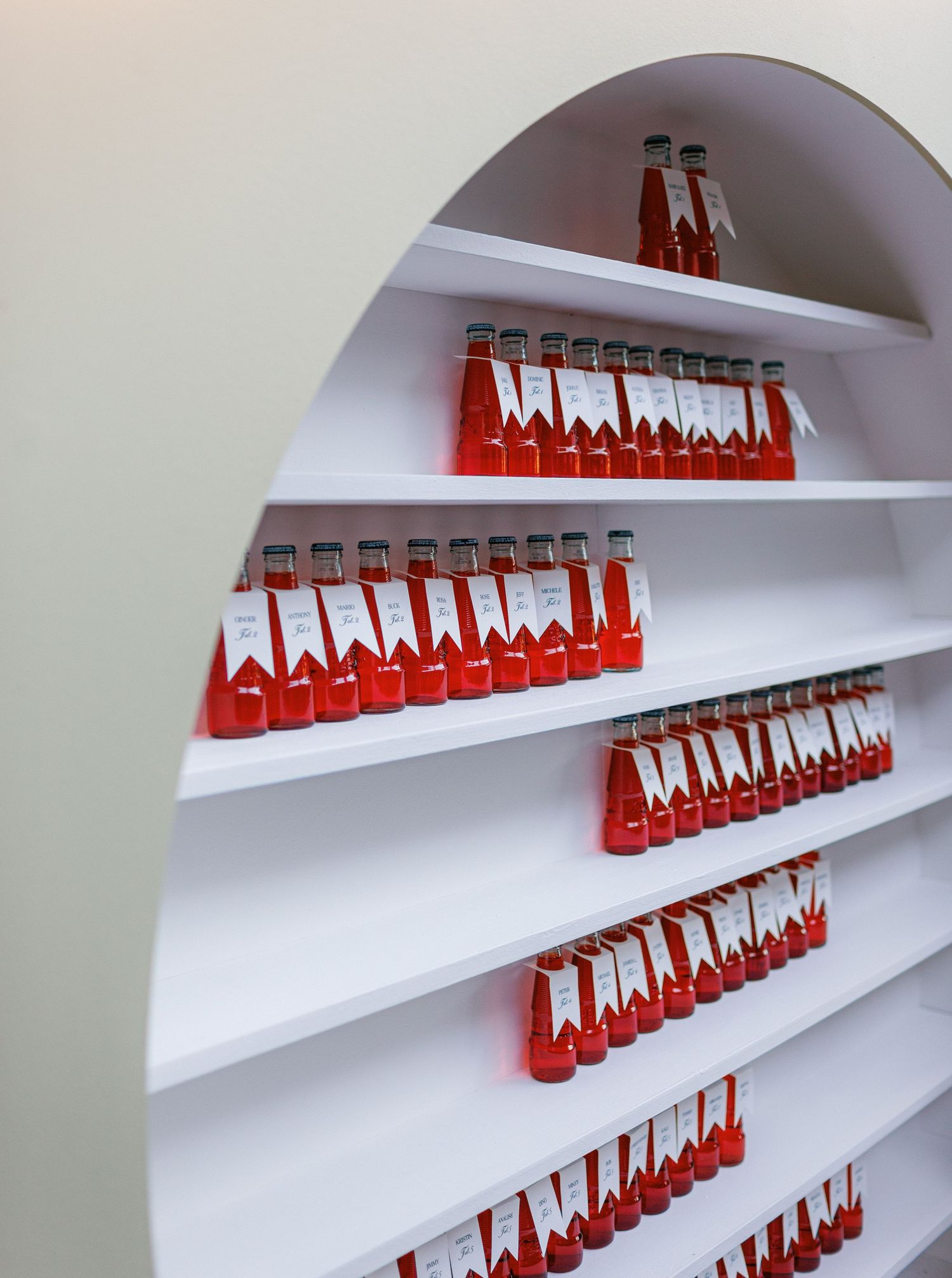 Red Coca-Cola bottles arranged in ascending diagonal lines on white shelves create a striking geometric display pattern.
