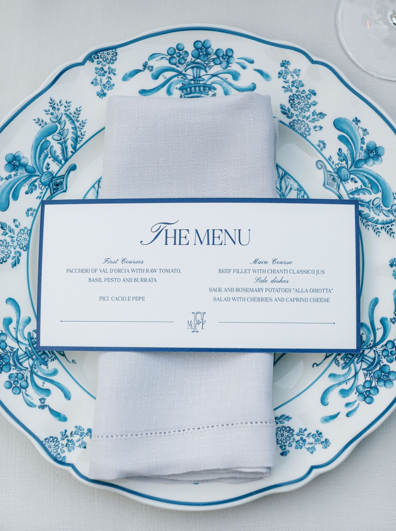 Elegant place setting with blue and white china plate featuring floral design and formal menu card.