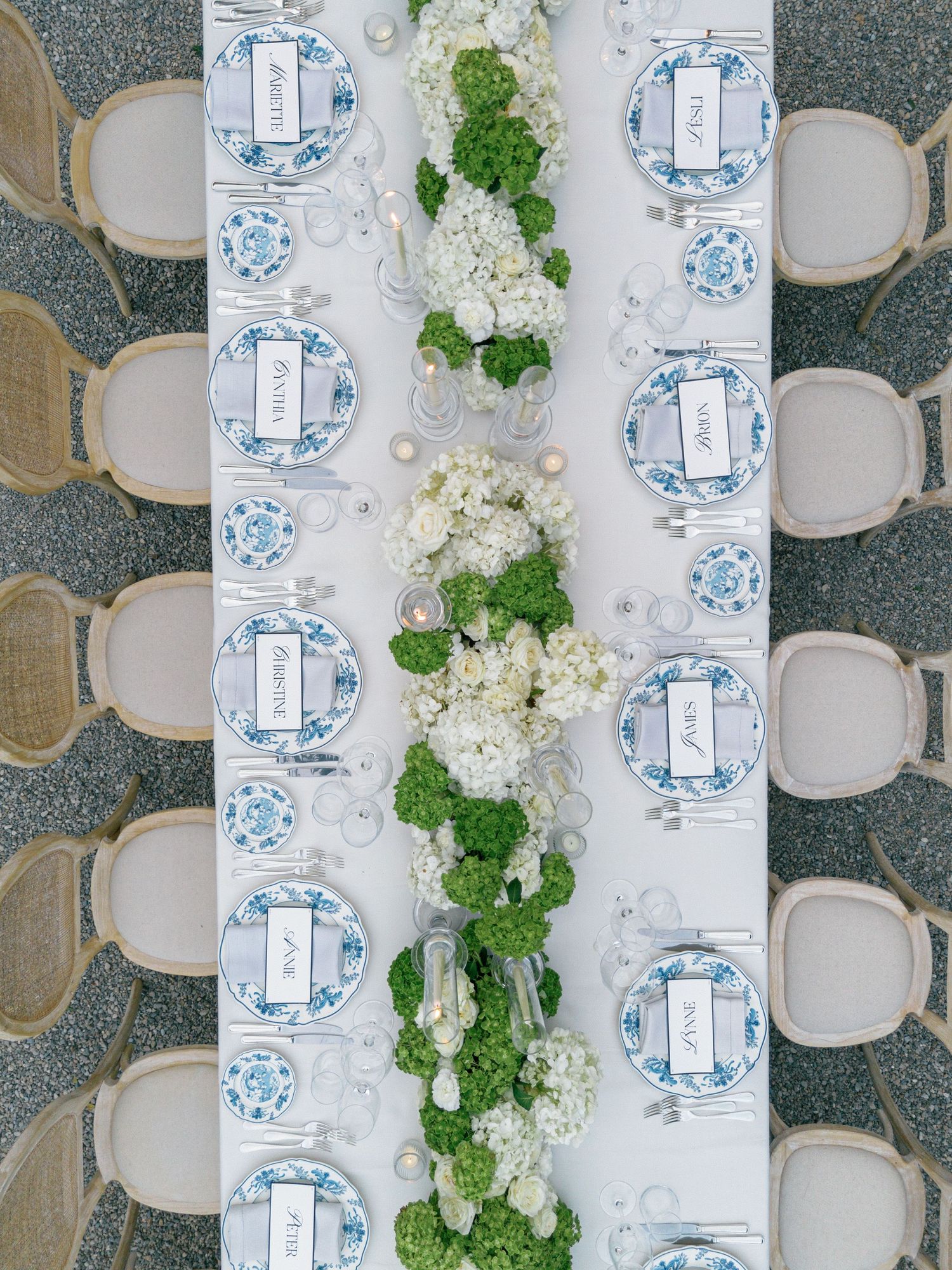 Bird's eye view of a formal dining table with blue and white china place settings and white floral centerpieces.
