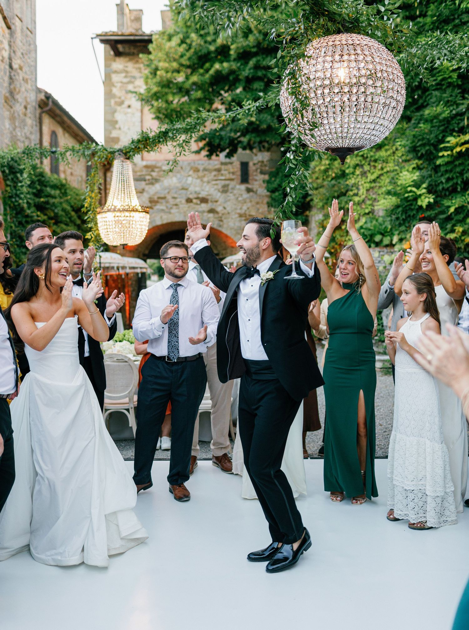 Wedding guests dancing and celebrating on an outdoor dance floor beneath crystal chandeliers at an elegant outdoor reception.