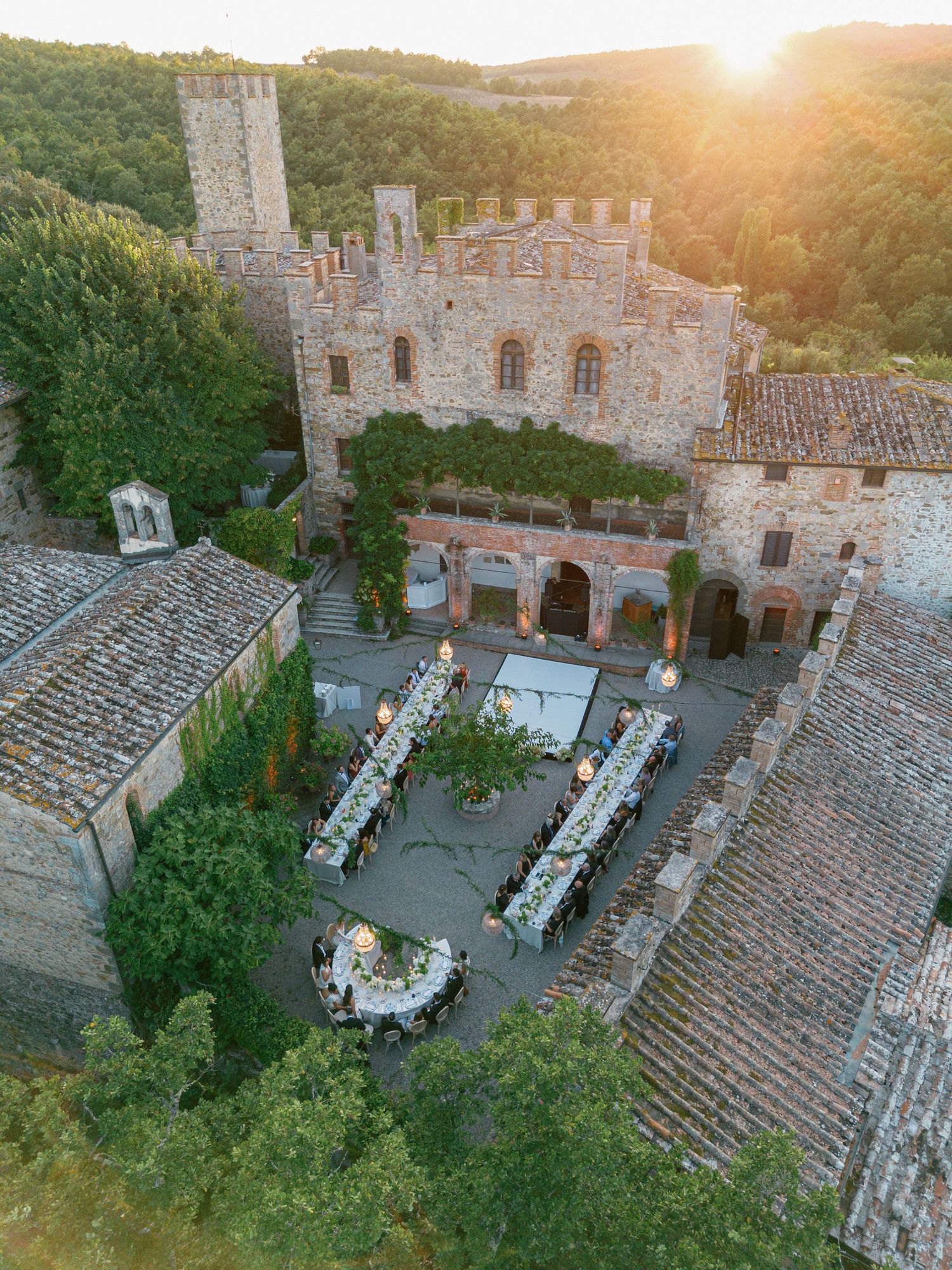 Aerial drone view of an elegant wedding reception setup in a rustic Italian courtyard at golden hour.