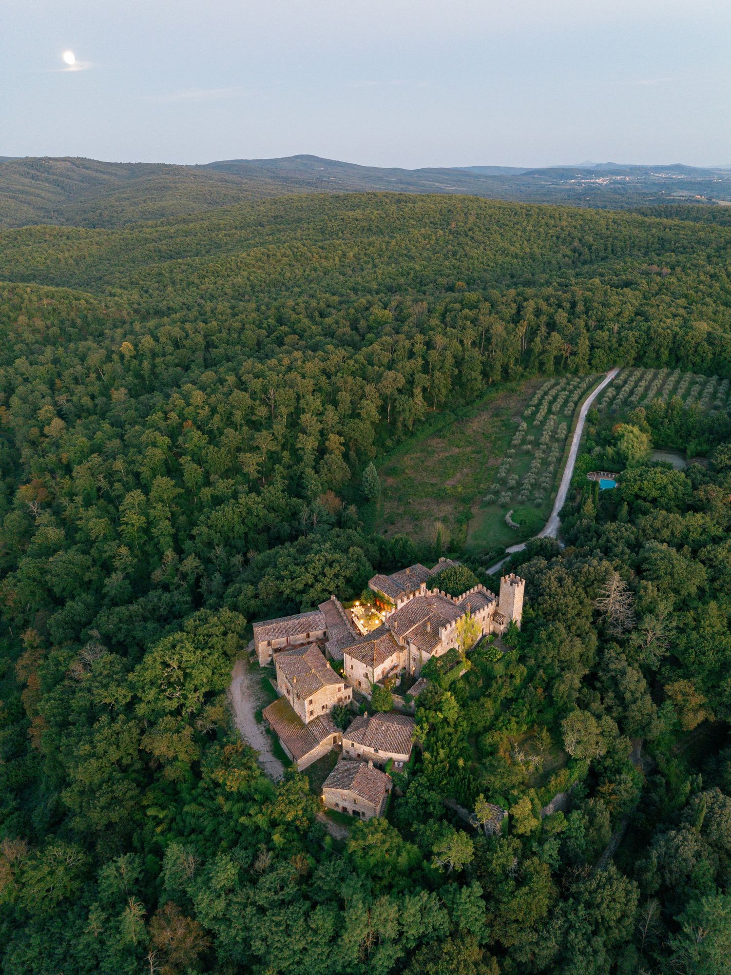 Aerial drone panorama of a historic monastery or castle complex nestled in dense forest with winding roads.