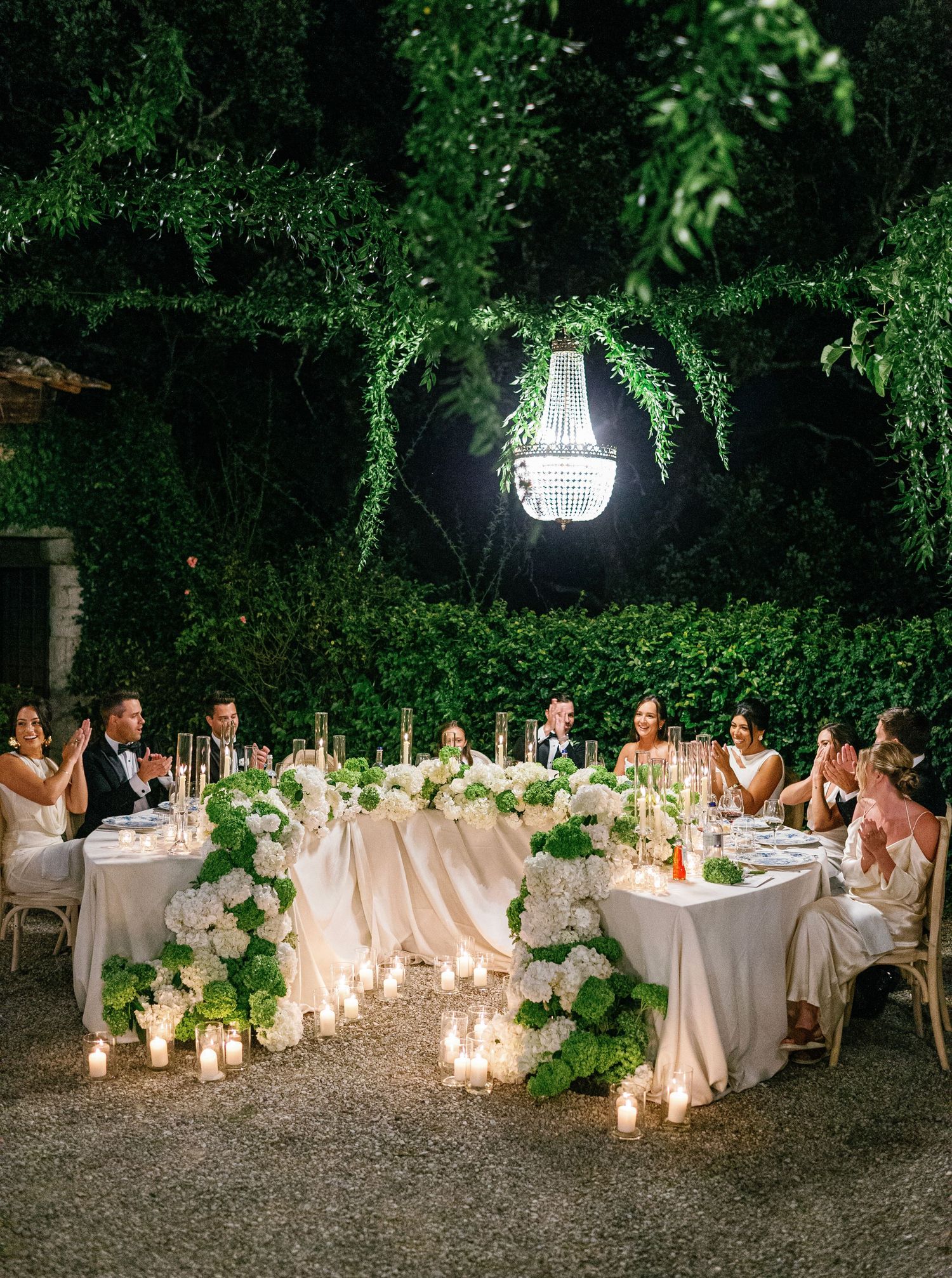 Elegant outdoor wedding reception setup with candlelit tables under trees and string lights creating a romantic atmosphere.