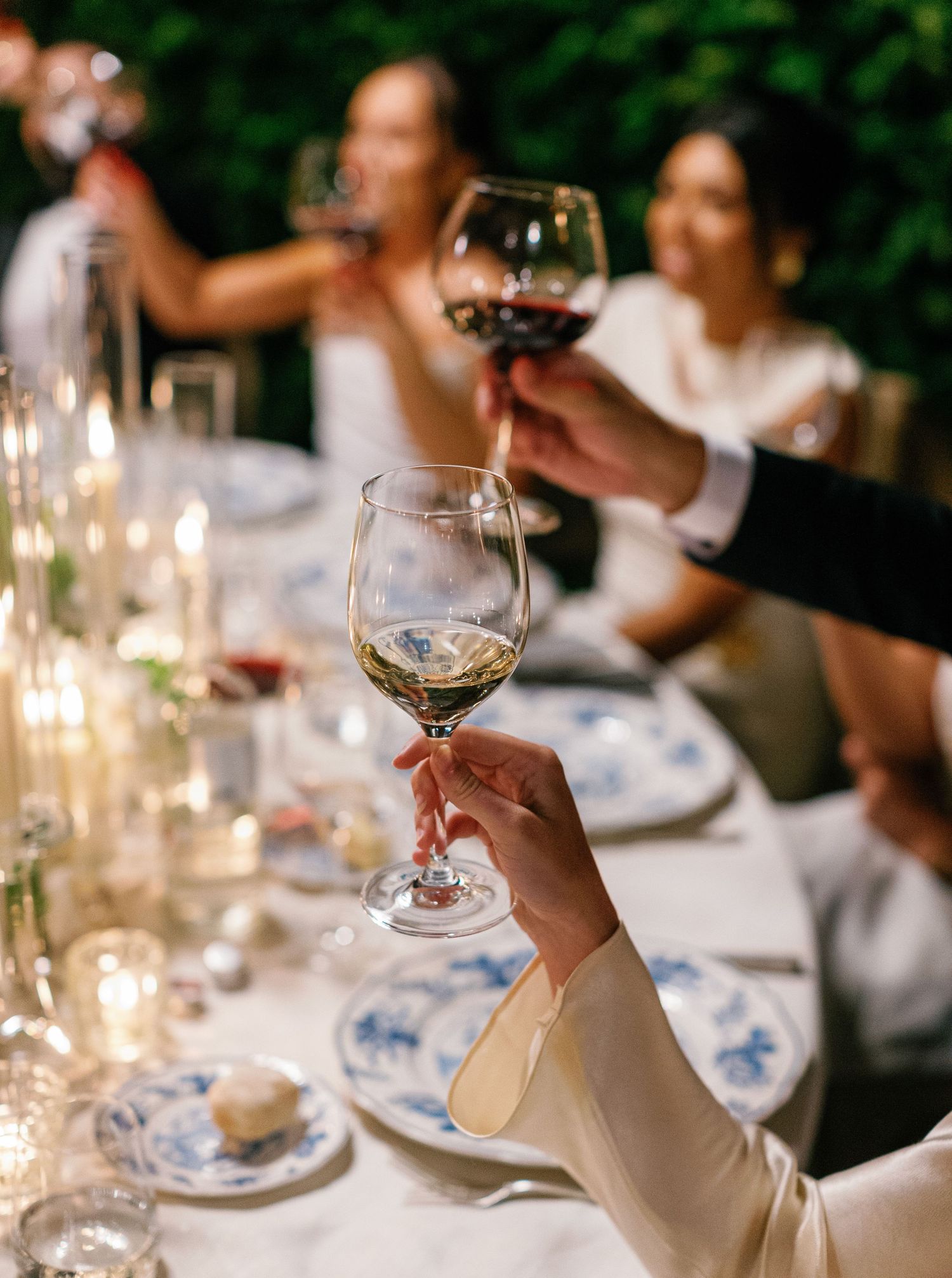 People enjoying wine and conversation at an elegant candlelit dinner table with blue and white china place settings.