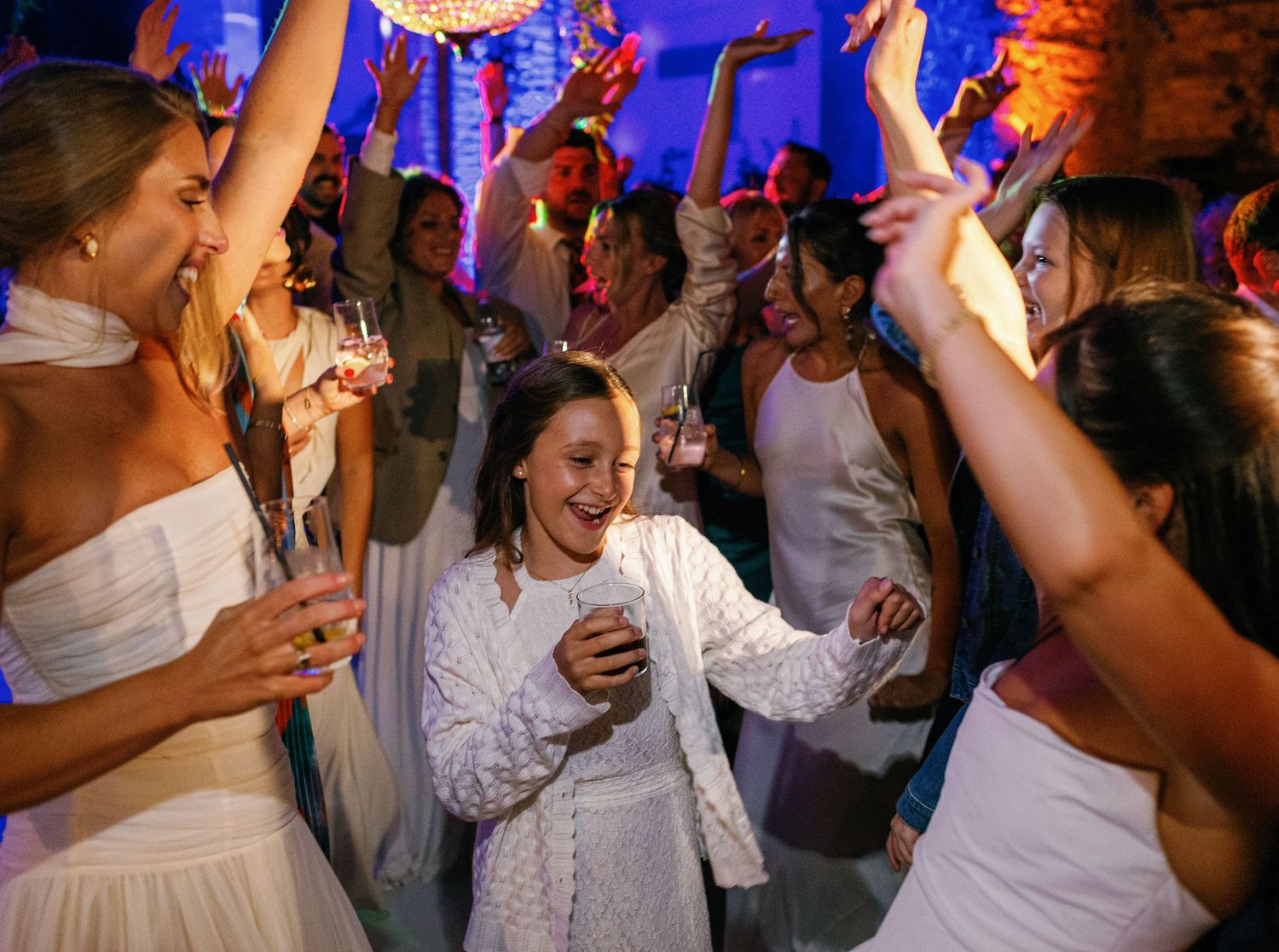 Wedding party guests dancing and celebrating on a dance floor with colorful blue lighting and festive atmosphere.