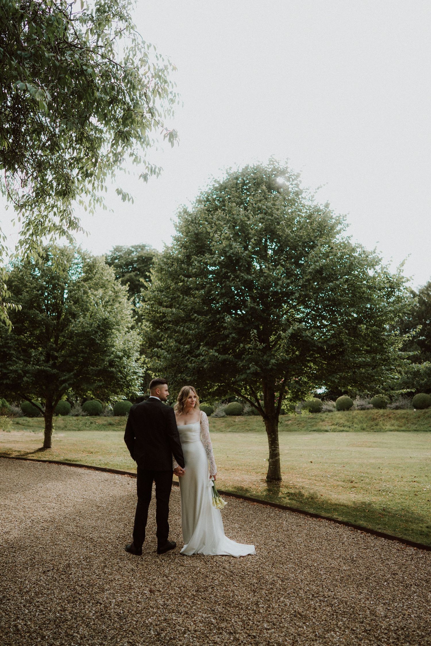 A couple walks together under trees in an orchard on their wedding day, creating a romantic outdoor scene at Sudeley Castle, Cotswolds