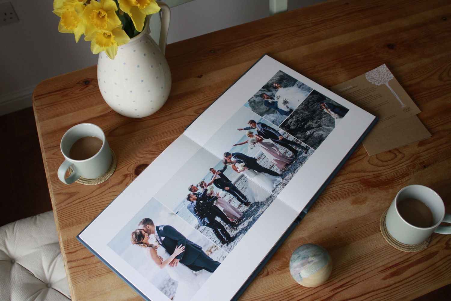 A collection of framed photos and coffee cups arranged on a rustic wooden table with yellow flowers in a vase.