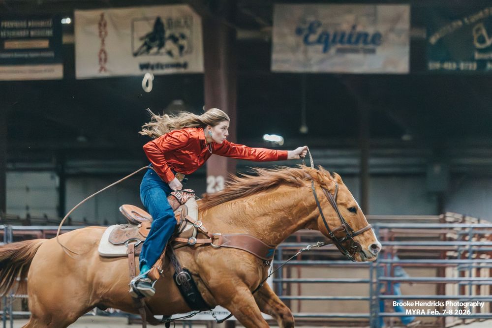 A rodeo rider competes on a palomino horse in an indoor arena during a barrel racing event.