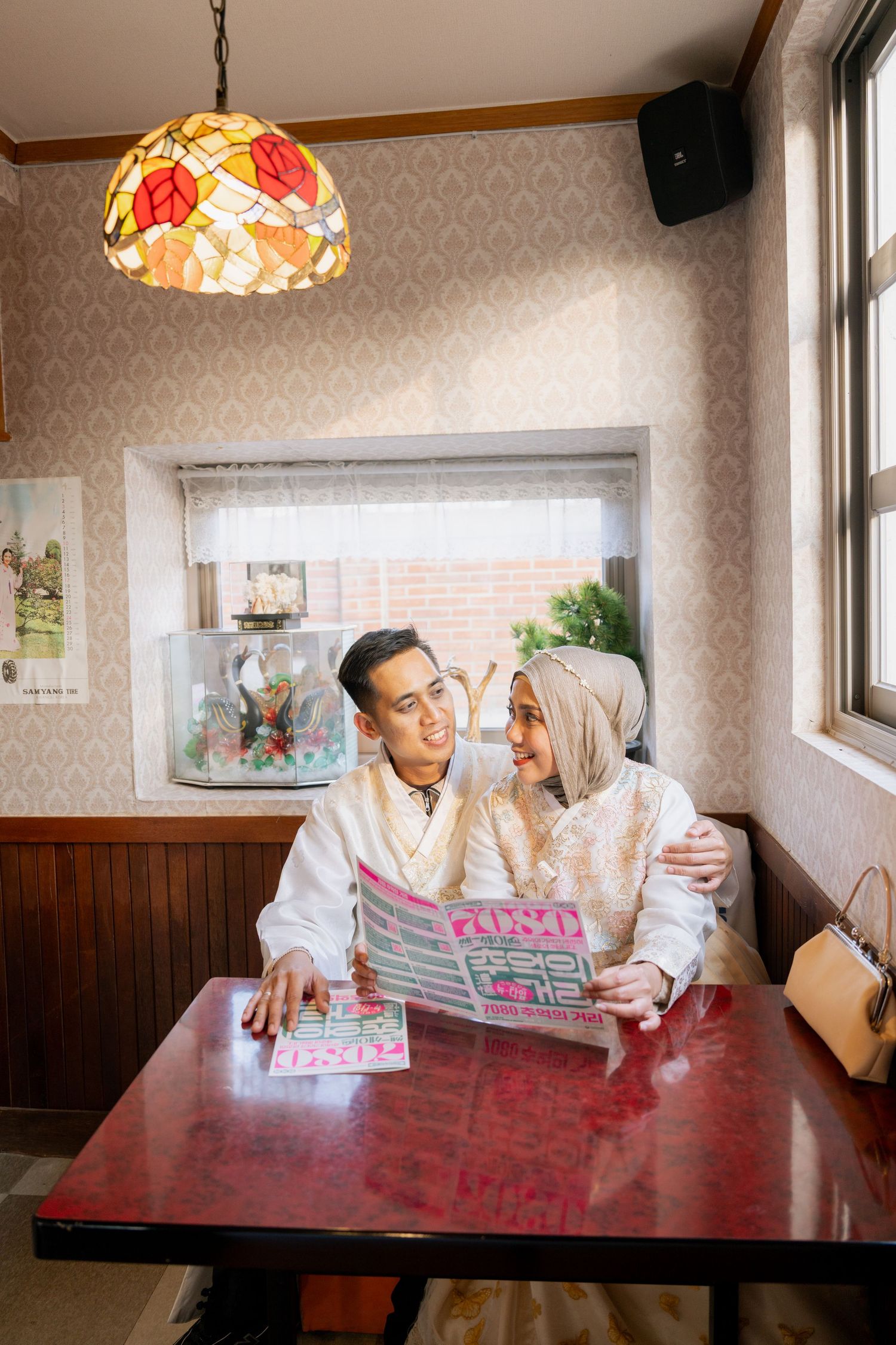 A couple shares a tender moment while reading together at a restaurant table under a decorative stained glass lamp.