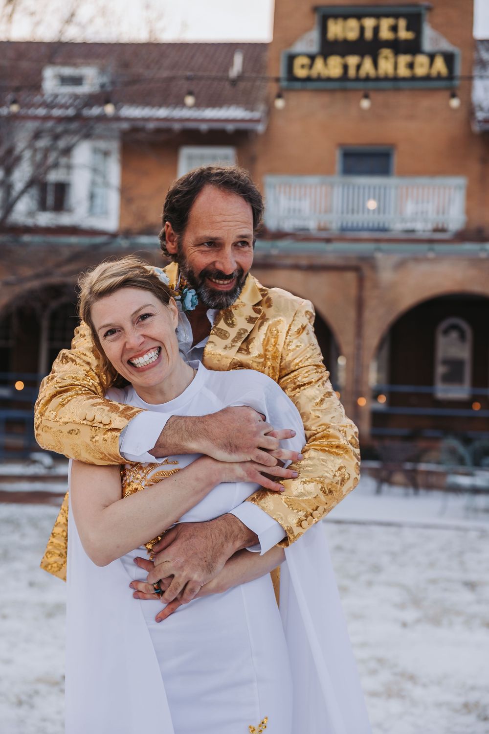 A couple embraces and laughs together in front of a hotel sign during a winter photoshoot.
