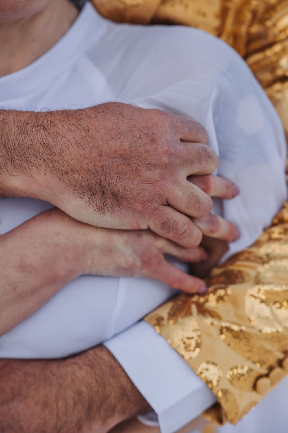 Close-up of hands crossed over a white shirt against a golden textured background.
