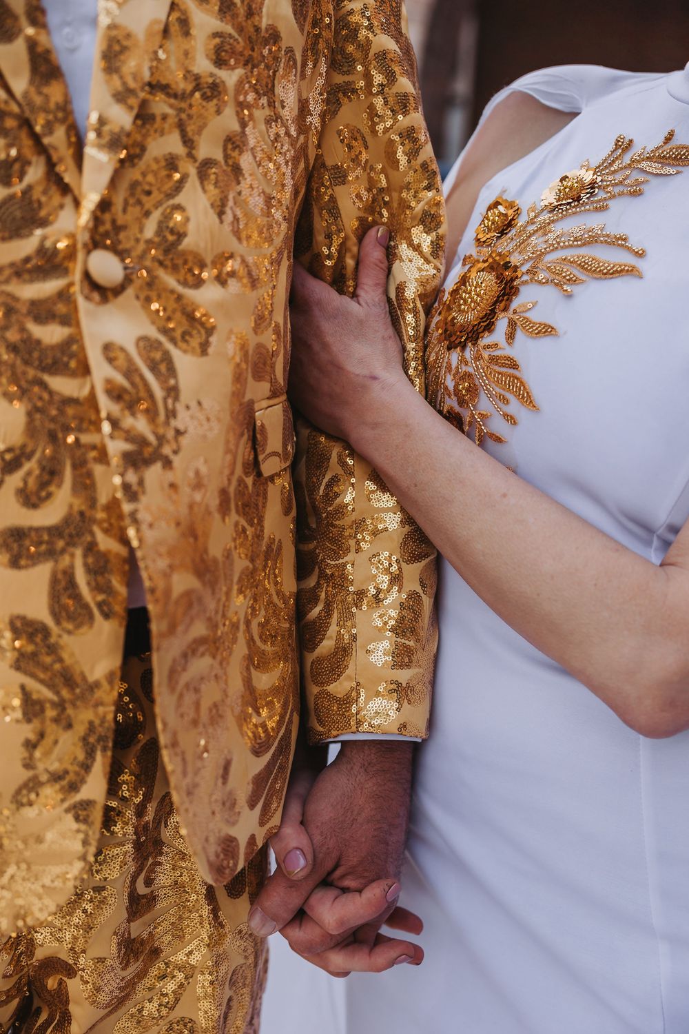 Close-up view of hands holding against golden floral embroidered fabric creating a romantic engagement photo.