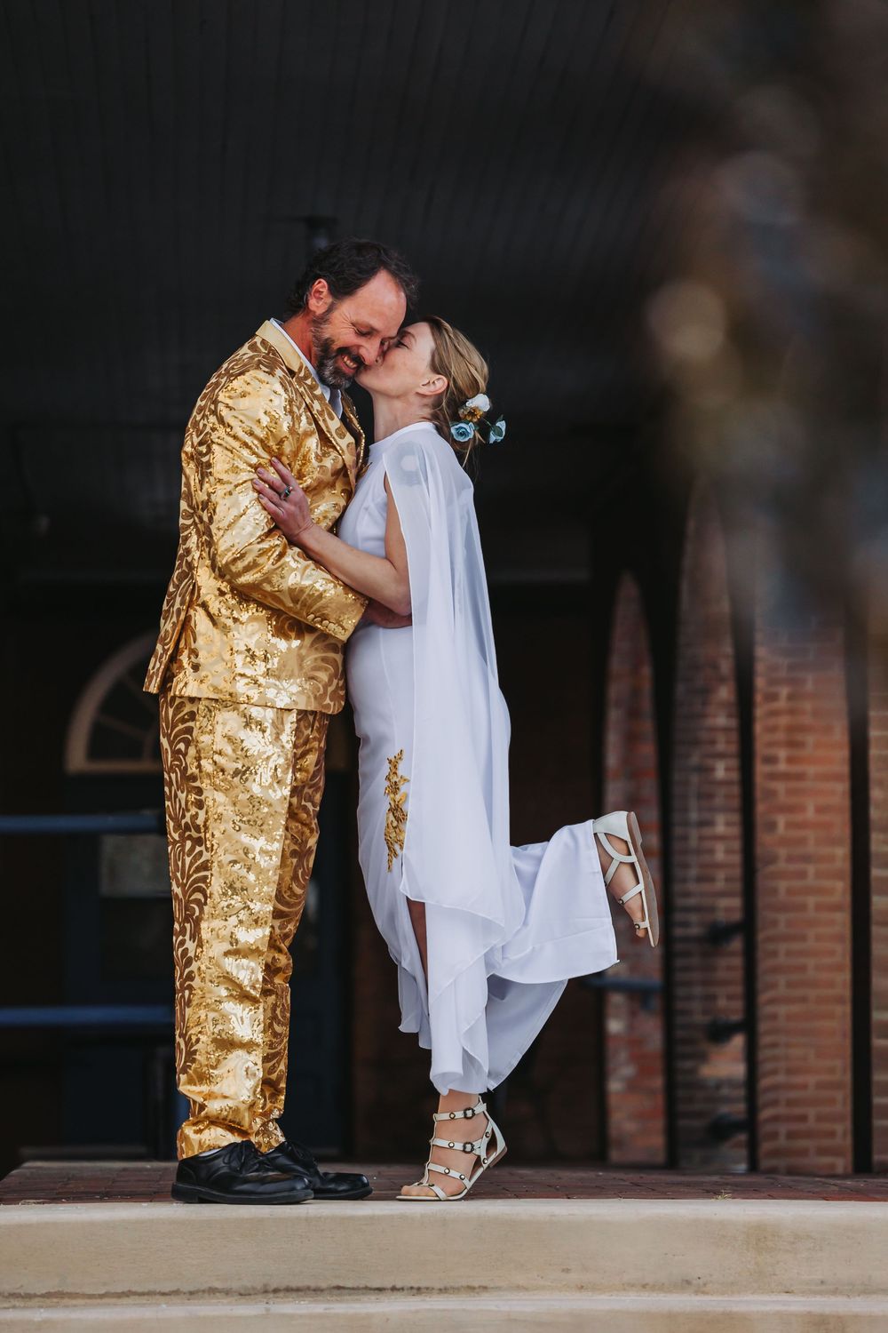 Two figures share an intimate moment, with one wearing a striking gold outfit and the other in white clothing.
