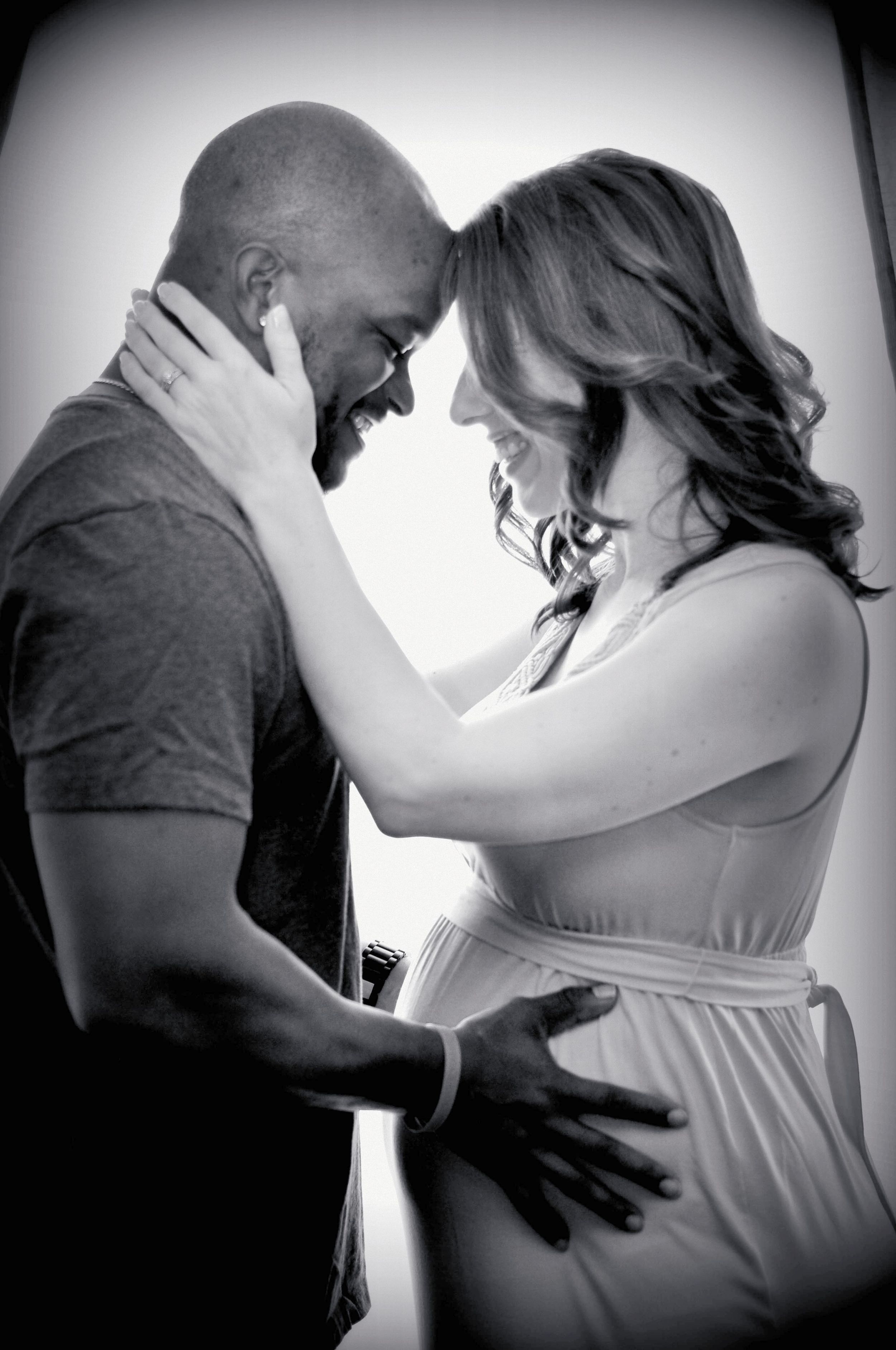A romantic black and white portrait of an interracial couple sharing an intimate maternity moment in soft lighting. Napa, California