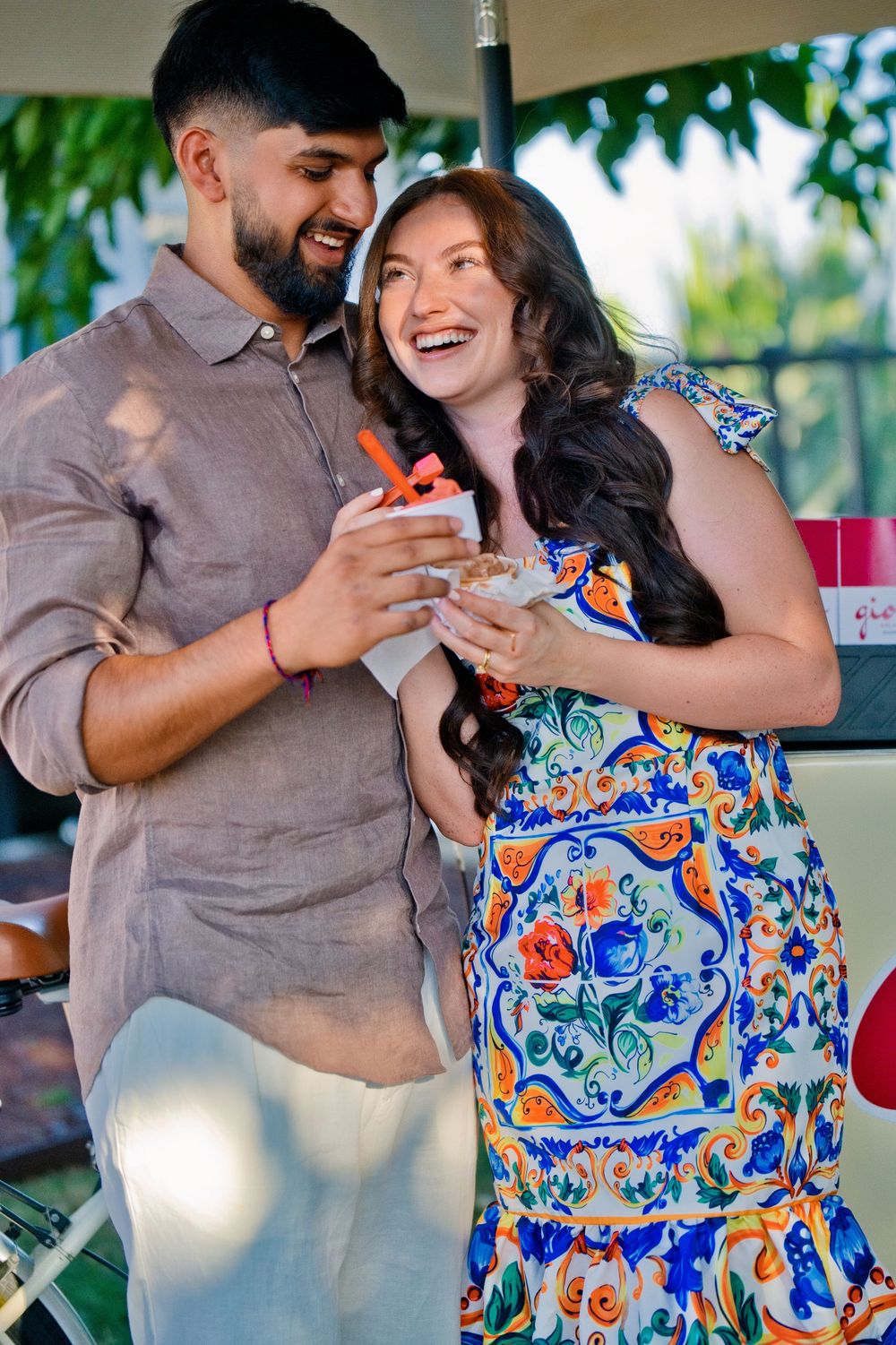A just engaged couple shares a joyful tender moment, the woman wearing a colorful floral dress and the man in brown. Surprise Proposal