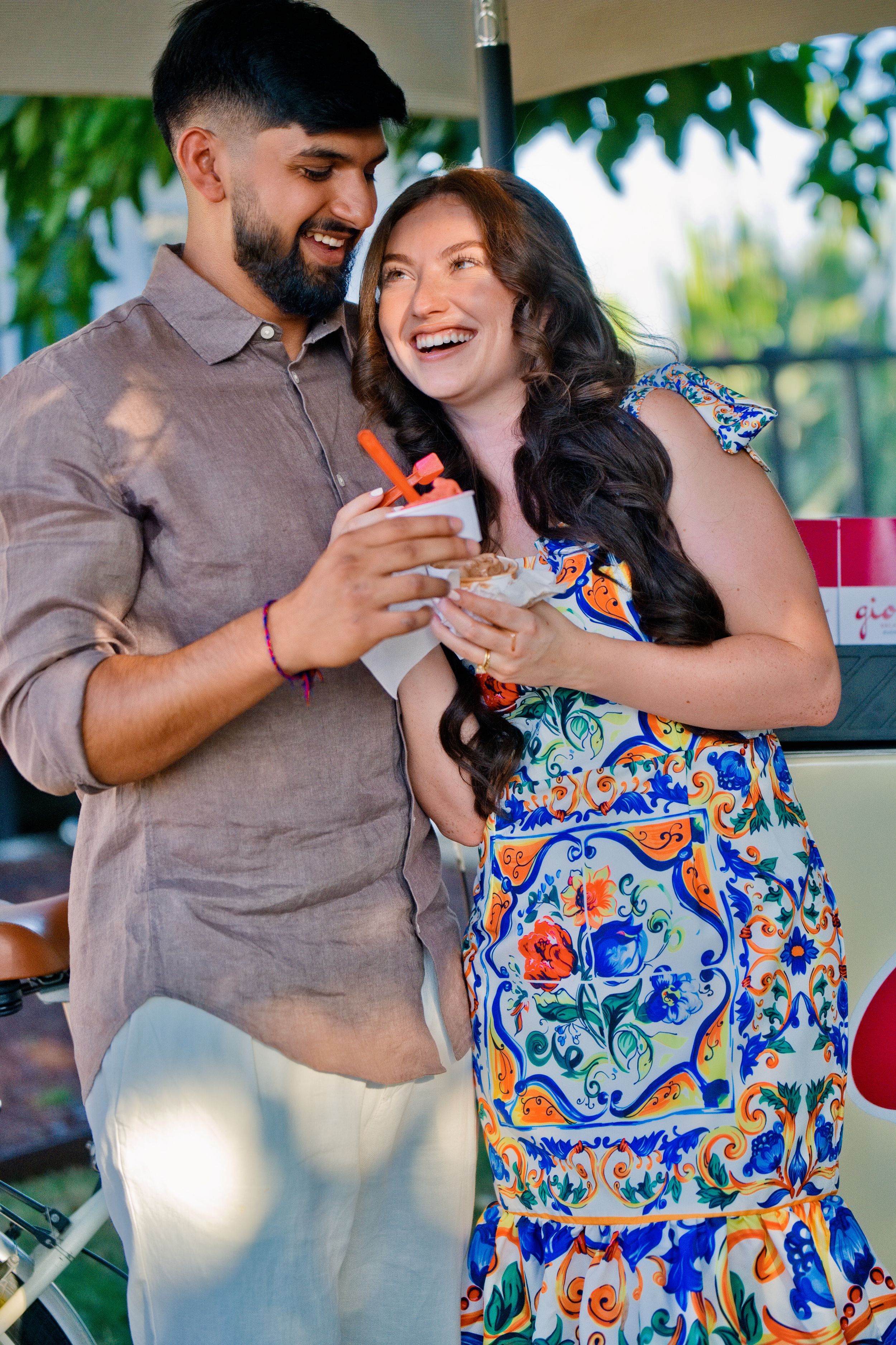 A just engaged couple shares a joyful tender moment, the woman wearing a colorful floral dress and the man in brown. Surprise Proposal