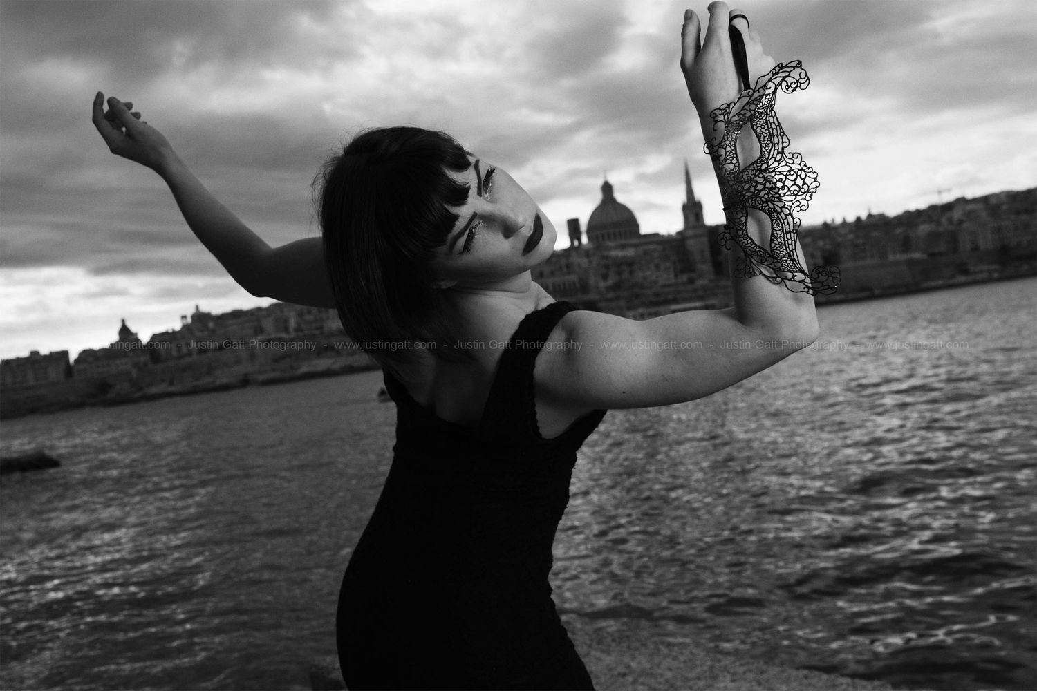 Silhouetted figure with raised arms against a dramatic cloudy sky by a river.