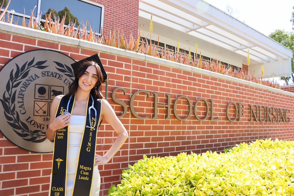 Students walking past red brick building entrance with yellow flowers blooming in landscaping.
