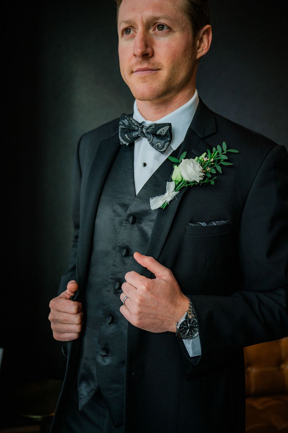 Close-up shots of a groom in a classic black tuxedo with white boutonniere and bow tie against dark background.