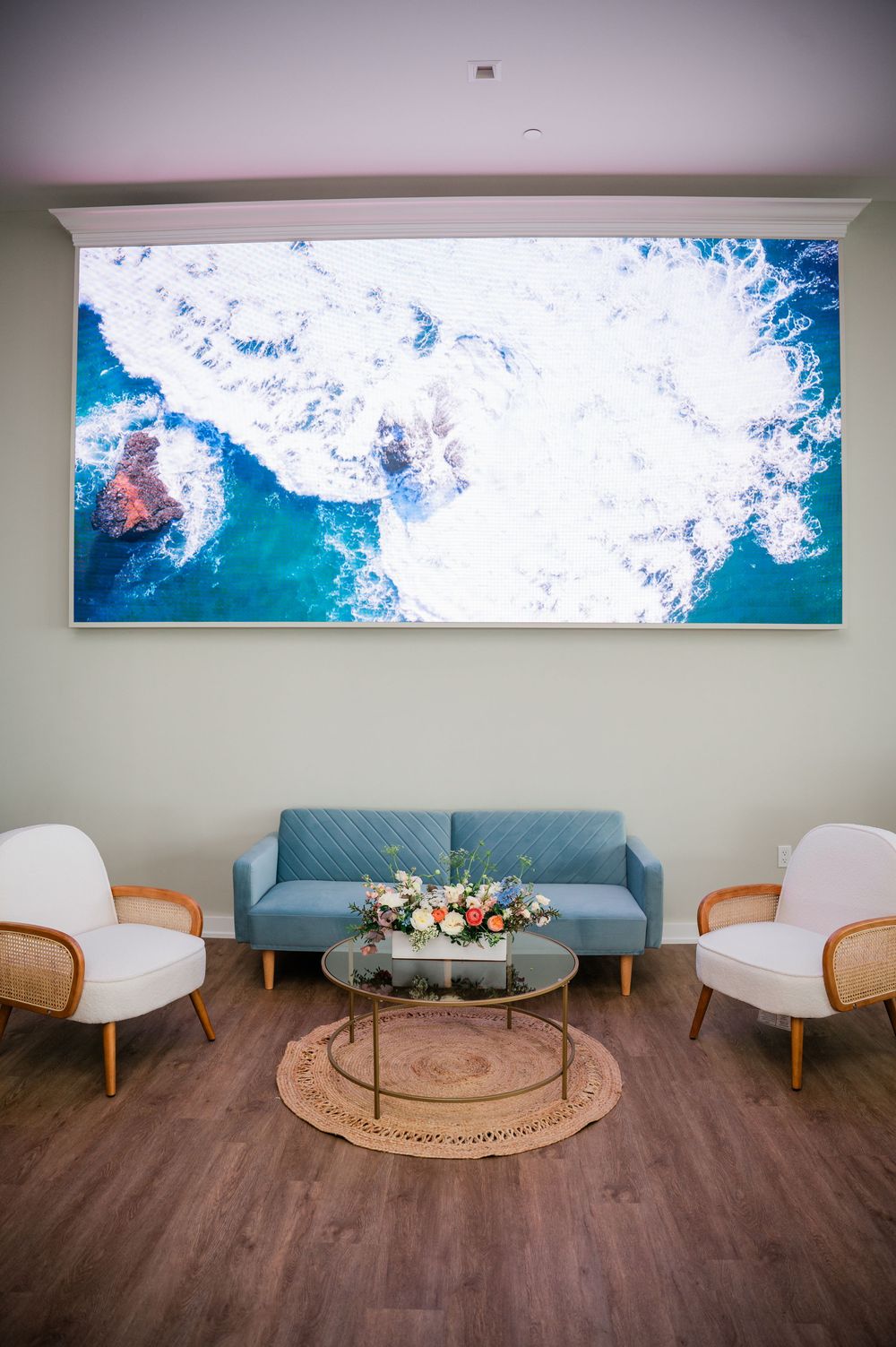 Modern waiting room interior with blue ocean artwork displayed above a light blue couch and wooden accent chairs.