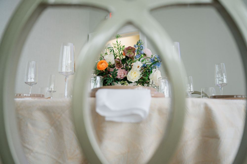 White floral arrangement viewed through an arched frame with glassware on an elegant table setting.