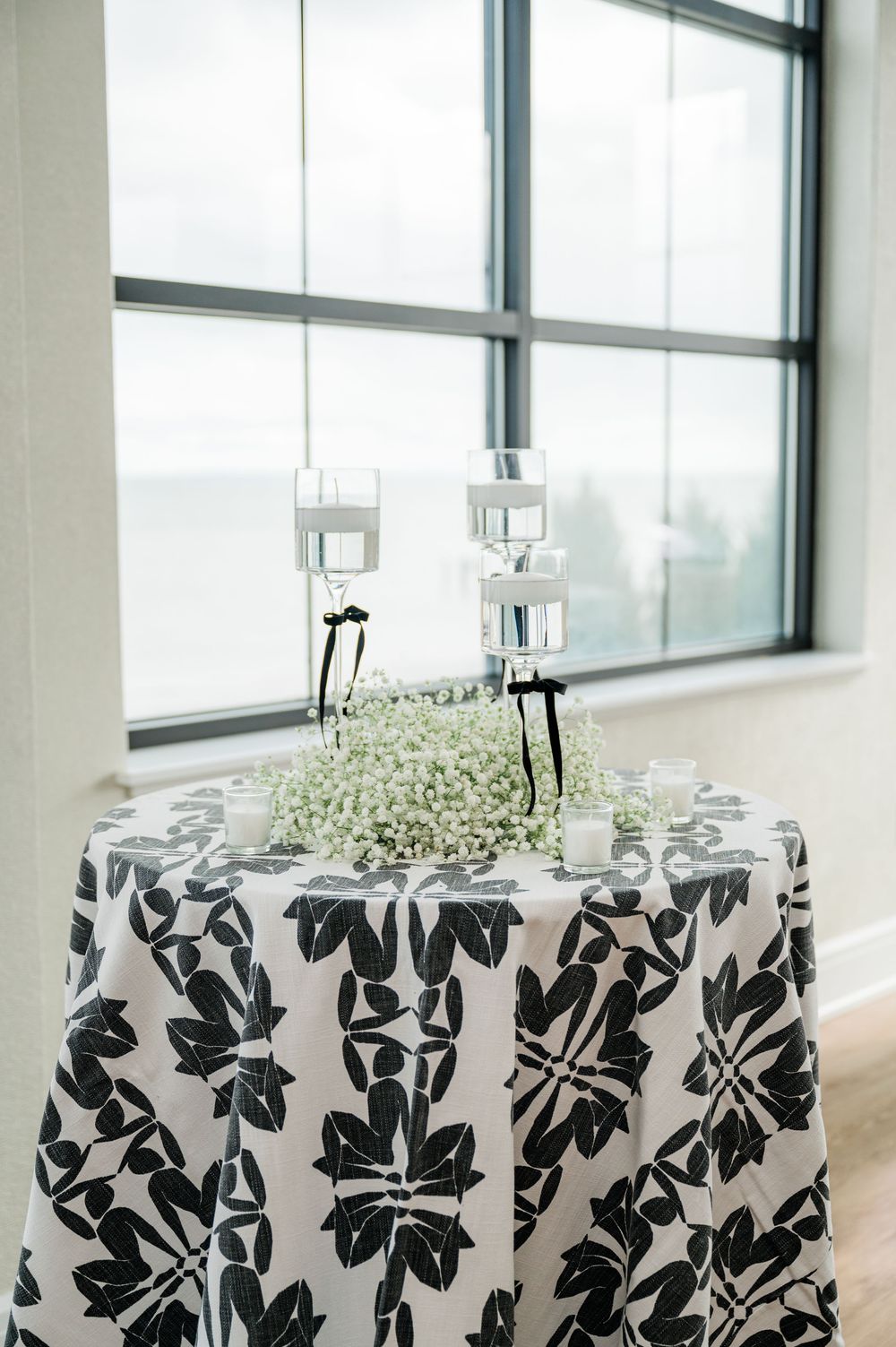 Modern wedding reception chairs with black and white floral print covers arranged in rows by large windows.