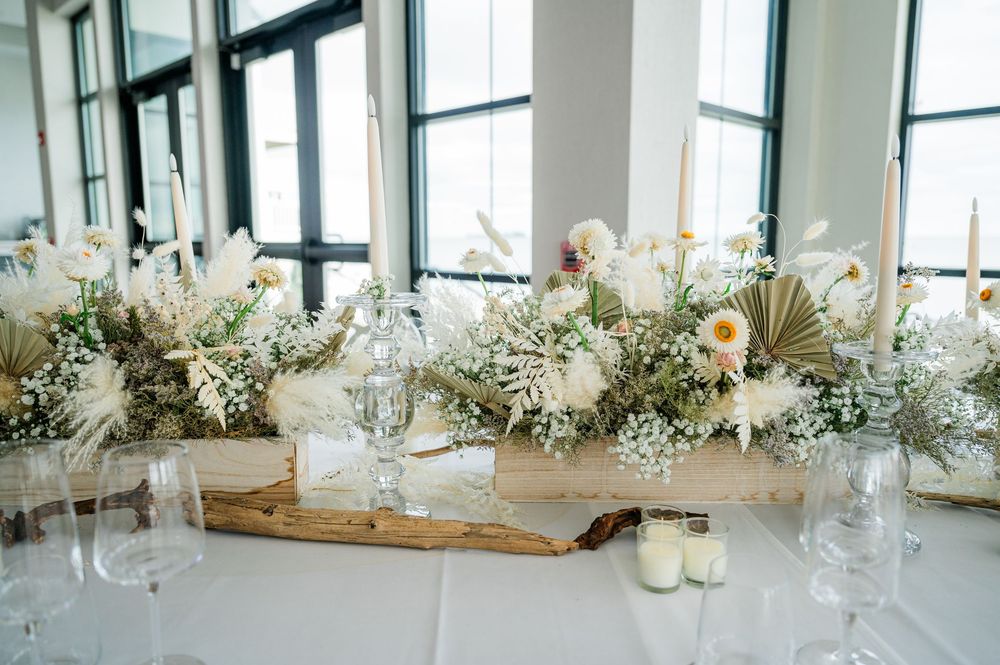 Elegant wedding reception table settings with white floral centerpieces and rustic wooden decor in natural light.