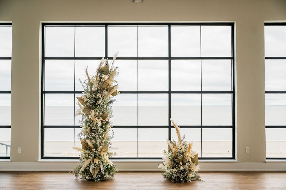 Two elegant floral arrangements with dried pampas grass and greenery stand against large modern windows in a bright room.