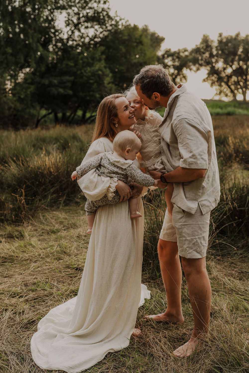 Happy family with two young children laughing together in a field during a warm sunset photo session.