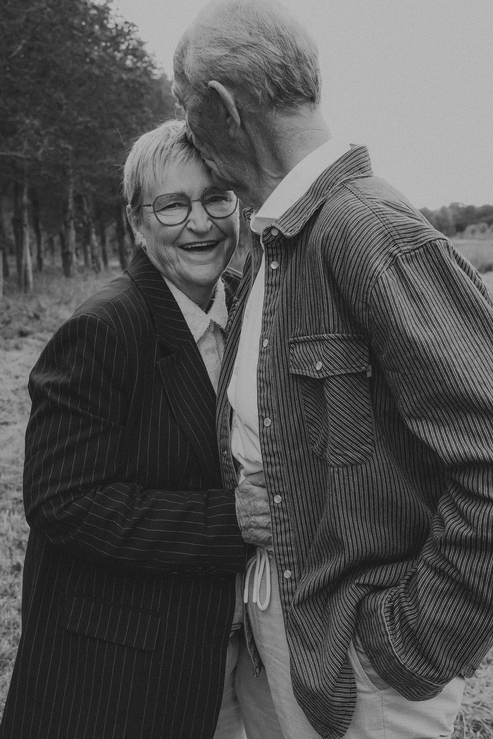 Black and white portrait of a joyful elderly couple sharing a loving moment outdoors in a field.