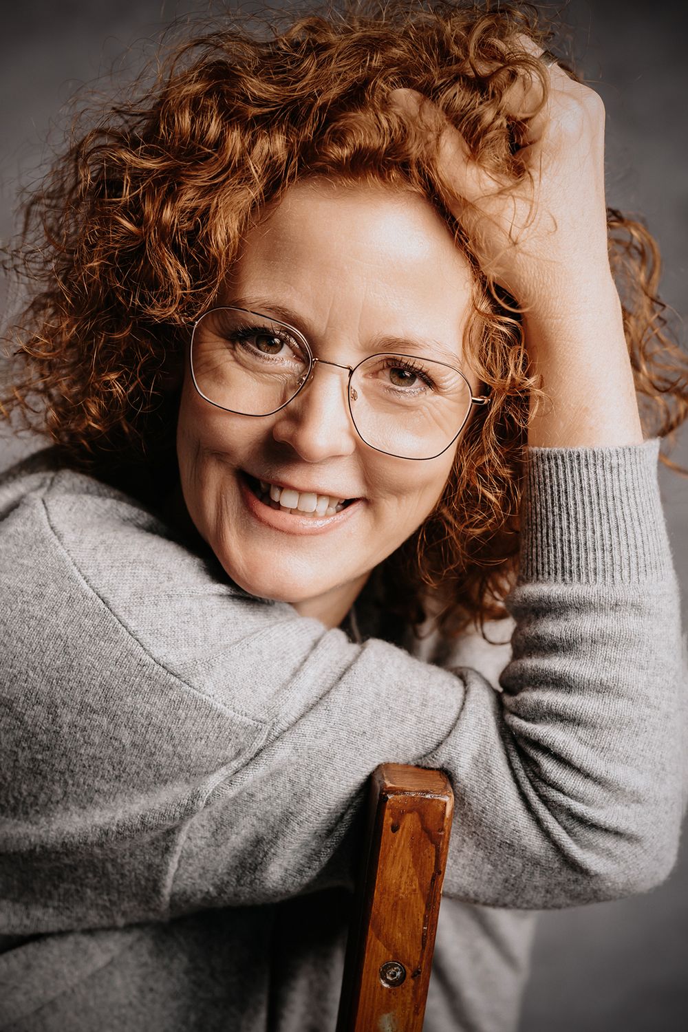 Frau mit roten Locken sitzt auf einem Stuhl, stützt sich auf, Hand in den Haaren, Nahaufnahme im Studio.