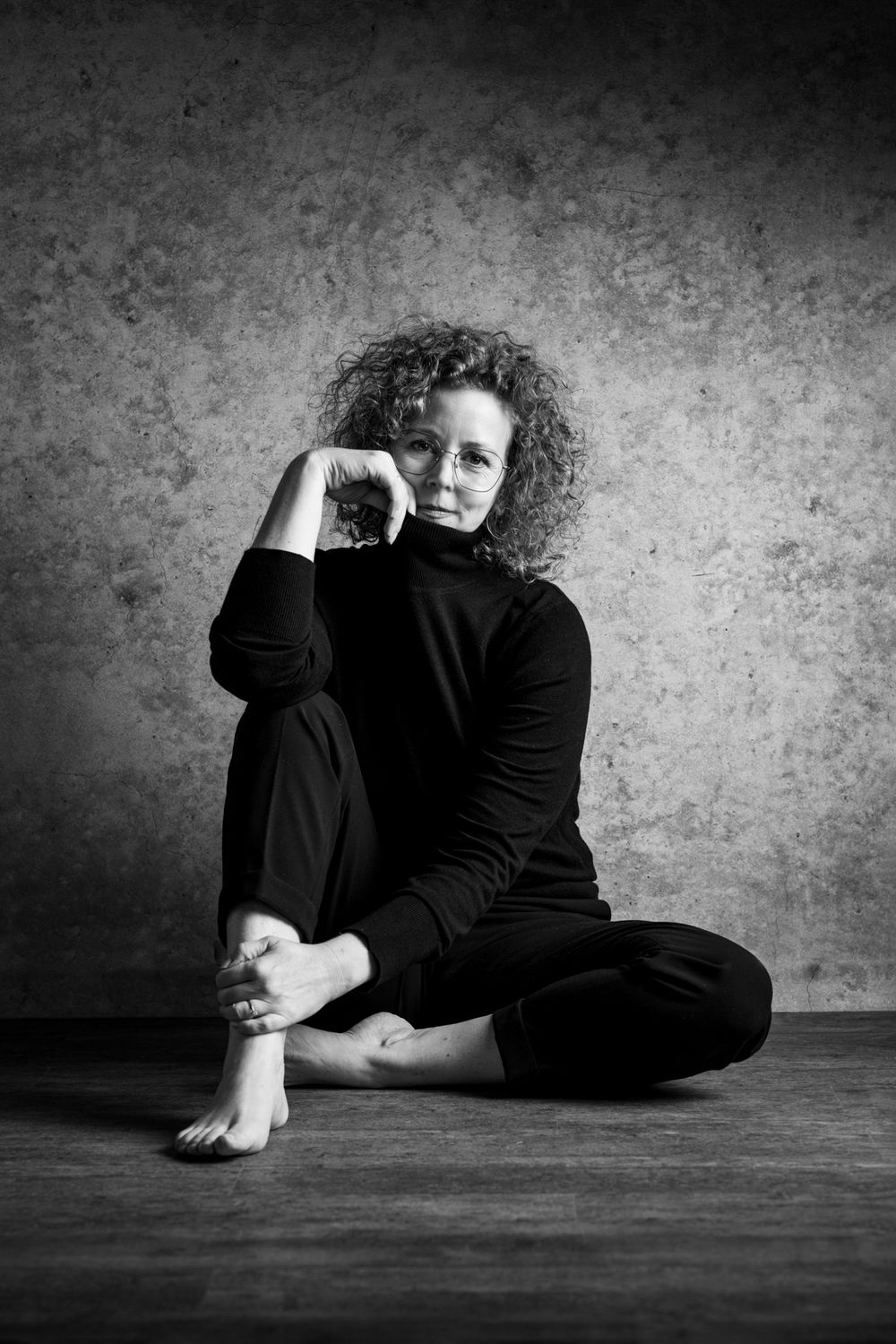 Schwarz-Weiß-Studioaufnahme einer Frau, sitzend an einer Betonwand, modernes Porträt im Fotostudio