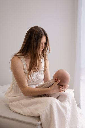 mum sitting down holding her newborn baby and looking at him during session in Bishopdale studio