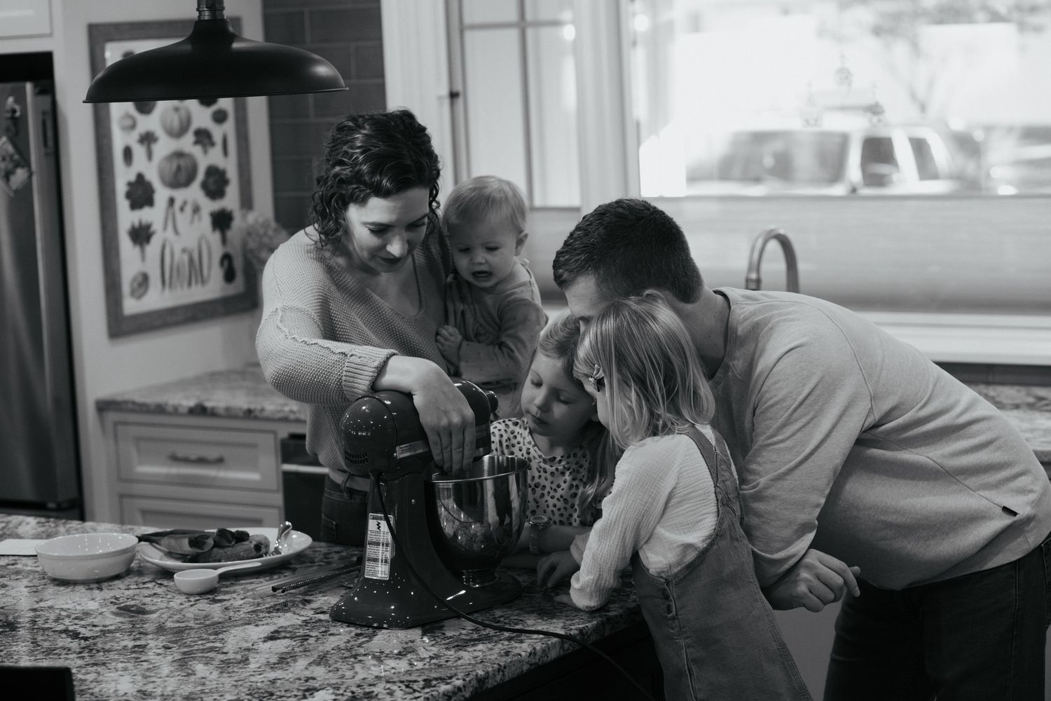 Black and white photo of family playing board game together at table.