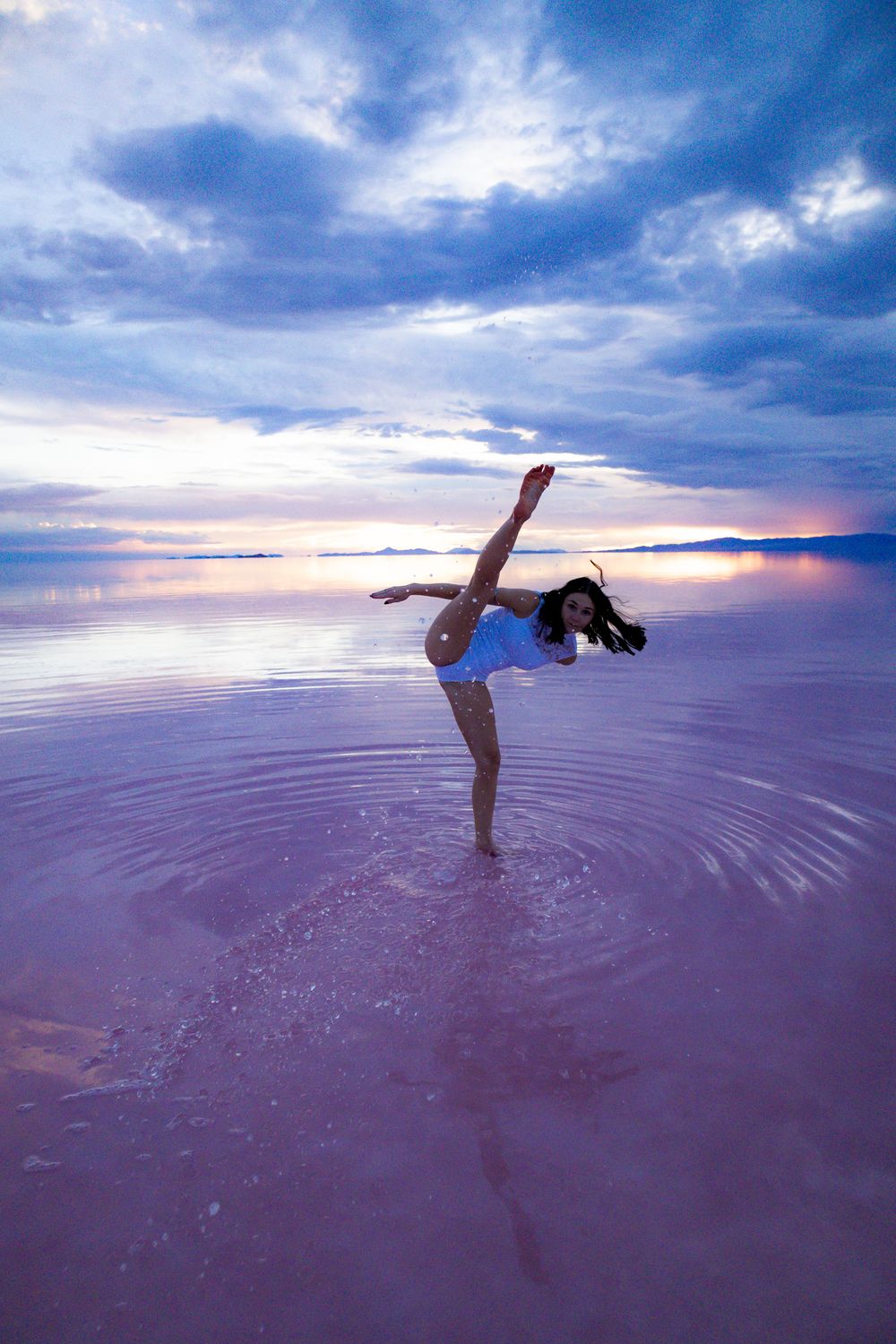 Artistic dance movements captured at sunset on reflective salt flat surface.