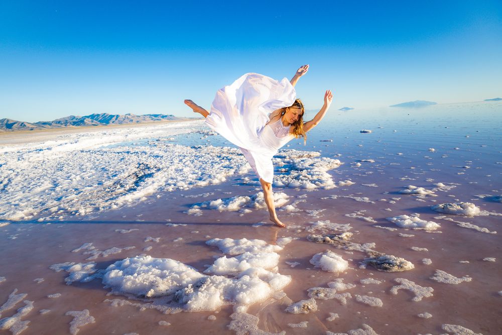 Elegant dance pose captured against dramatic salt flat landscape at sunset.