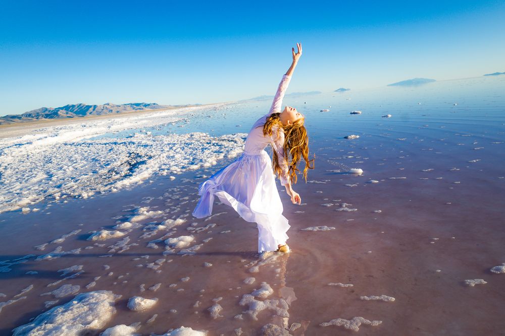 Dynamic dance movement photographed on reflective salt flats with mountains in distance.