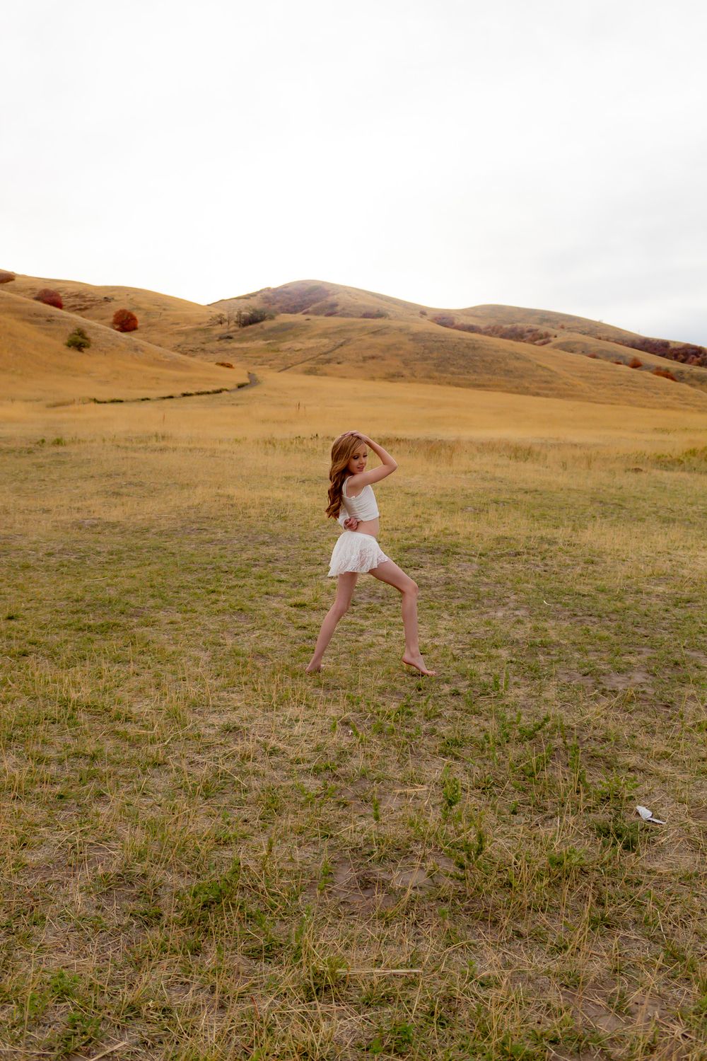 A dancer moves gracefully in a white outfit against a backdrop of rolling autumn hills.