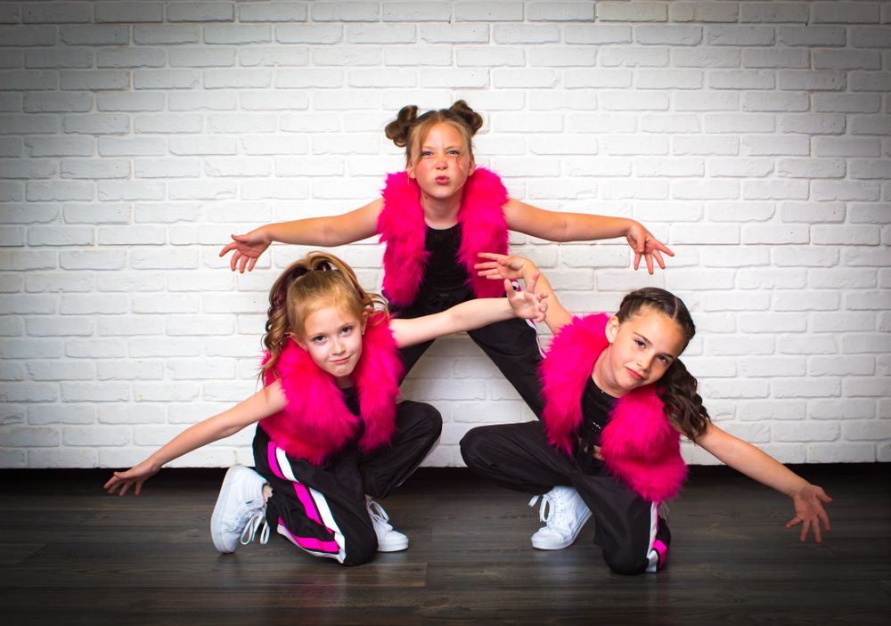 Energetic dance sequence in pink and black outfits against white brick wall.