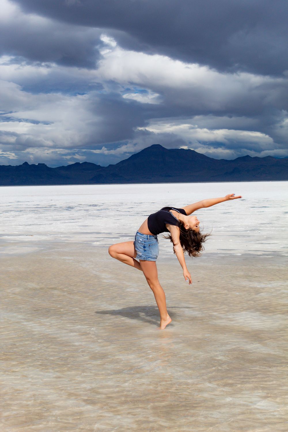 Expressive dance pose on salt flats showcases fluid movement against mountain landscape.