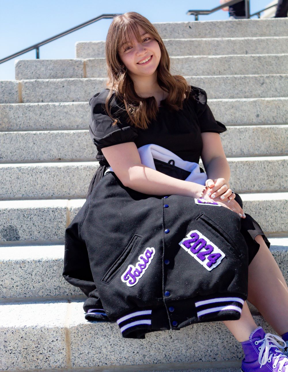 Person lounging on gray stone steps wearing black dress and purple shoes.